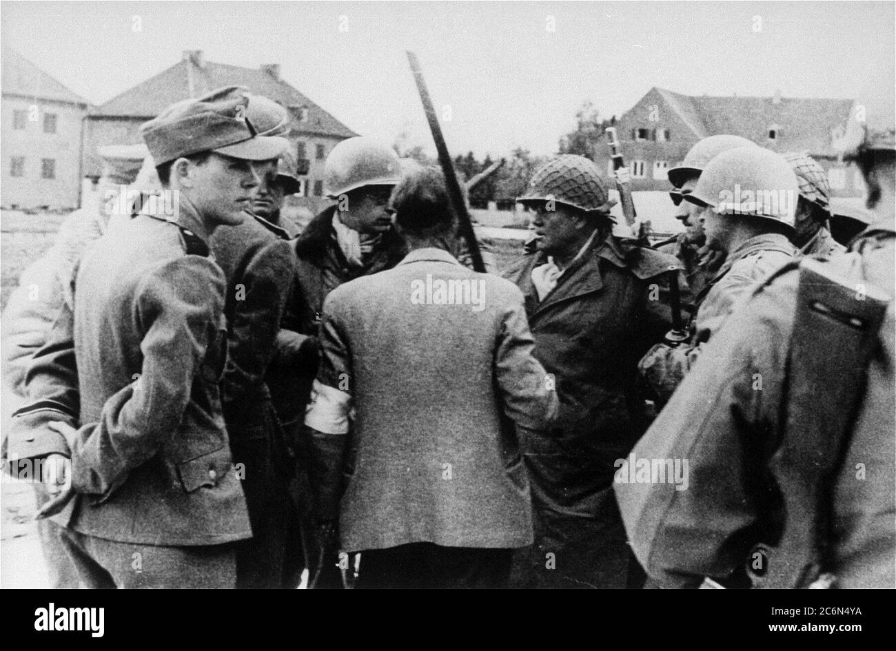 Die Übergabe des Konzentrationslagers Dachau an amerikanische Streitkräfte der 42. Infanterie-Division der Armee, 29. April 1945 in Dachau, Deutschland. Von links nach rechts sind abgebildet: Ein Helfer der Nazi-SS LT. Wickert, der das Lager aufgegeben hat; LT. Wickert (teilweise von seinem Adjutanten versteckt); Paul M.G. Levy, ein belgischer Journalist, der als Dolmetscher tätig war; Dr. Victor Maurer (zurück zur Kamera), der Delegierte des Internationalen Roten Kreuzes, der die Bedingungen für die Kapitulation arrangierte; 42. Stellvertretender Kommandant der Infanteriedivision Brig. Gen. Henning Linden; Linden Leibwächter. Maurer hält eine provisorische Flagge der Kapitulation Stockfoto