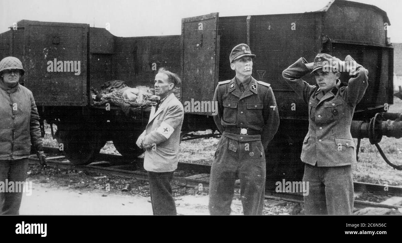 Die Übergabe des Konzentrationslagers Dachau an amerikanische Streitkräfte der 42. Infanterie-Division der Armee, 29. April 1945 in Dachau, Deutschland. Der deutsche Offizier, der als Kommandant des Lagers dient, zweiter von rechts, SS-Oberstleutnant Heinrich Wickert (Wicker), wird rechts von dem Schweizer Vertreter des Internationalen Roten Kreuzes, Dr. Victor Maurer, begleitet. Die Gruppe wurde neben dem „Todeszug“ von Triebwagen fotografiert, die die Toten der vor der Lagerübergabe nach Dachau überführten Personen hielten. Amerikanische Soldaten der 7. Armee der USA, einschließlich der 42. Infanterie und 45. Infanterie und 20. Panzerdivisionen Stockfoto