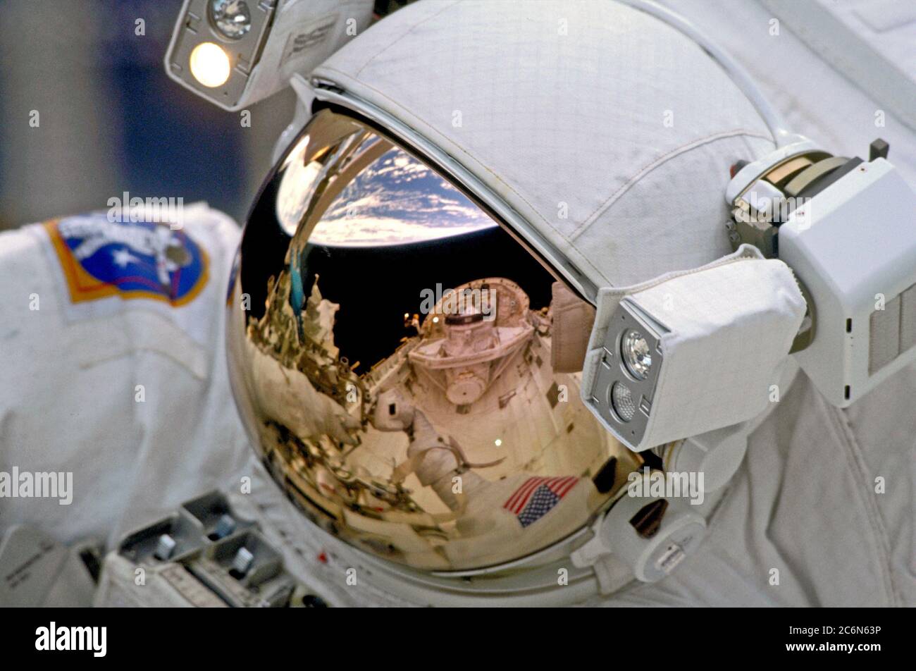 (19. - 27. Dezember 1999) - das Cargo Bay and Crew Module des Space Shuttle Discovery und der Horizont der Erde spiegeln sich im Helmvisier eines der Weltraumastronauten auf STS-103 wider. Die Astronauten Steven L. Smith, John M. Grunsfeld, C. Michael Foale und Claude Nicollier nahmen an drei Tagen an der dritten Inspektion des Hubble Space Telescope (HST) der NASA Teil. Stockfoto