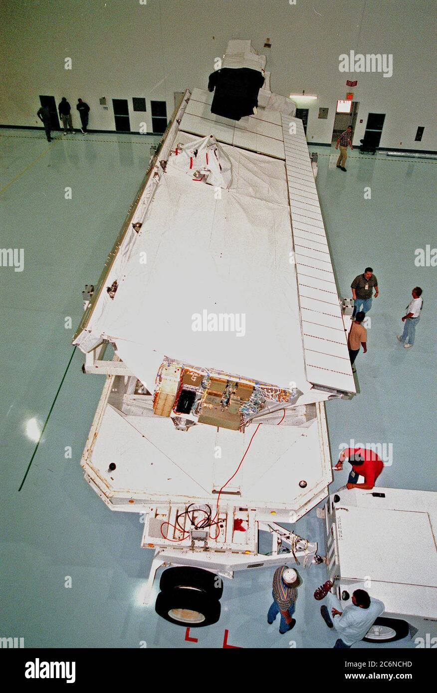 In der Raumstation Processing Facility (SSPF) trennen Arbeiter (unten rechts) das Transportfahrzeug von der Shuttle Radar Topography Mission (SRTM), nachdem sie es für die Vorbereitungen vor dem Start in das Gebäude gebracht haben. Stockfoto
