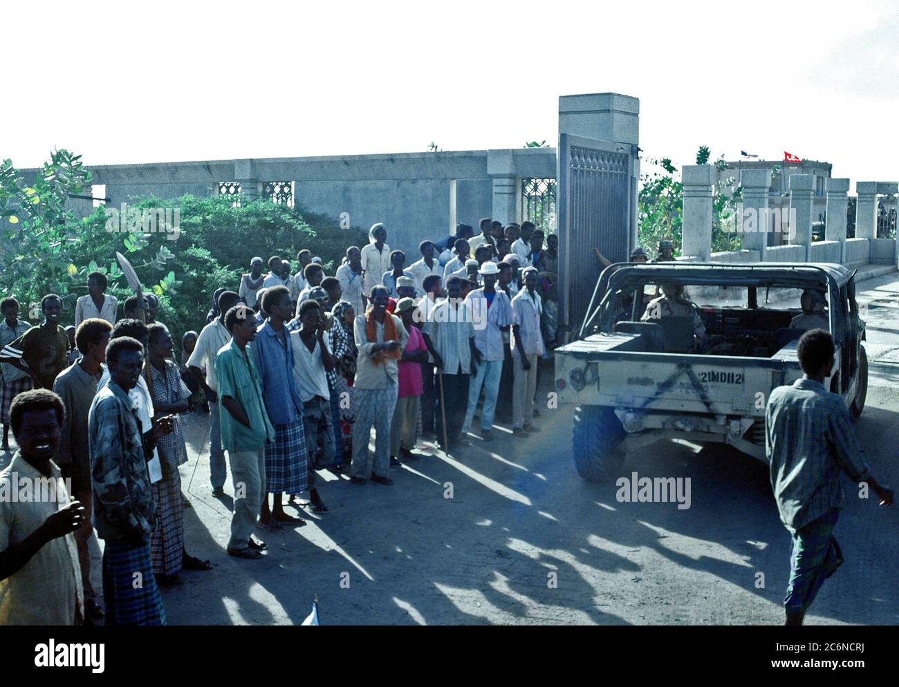 1992 - Somalis zusehen, wie ein M-998 Serie Fahrzeug der Joint Task Force Somalia Sitz tritt. Der Sitz wurde auf der ehemaligen US-Botschaft während der multinationalen Entlastung Bemühung Operation Restore Hope gegründet. Stockfoto