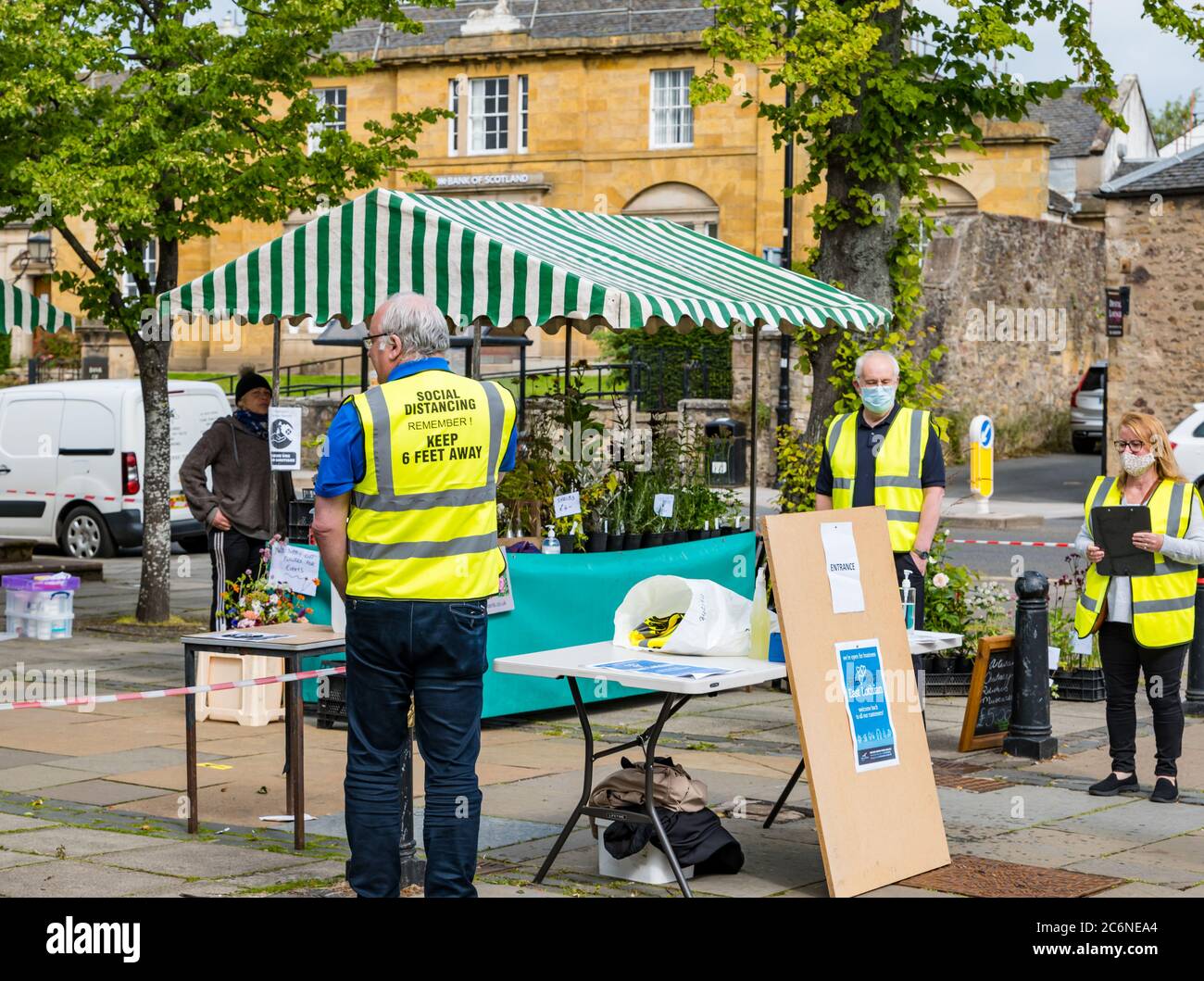 Haddington, East Lothian, Schottland, Großbritannien, 11. Juli 2020. Bauernmarkt startet in Phase 3 wieder: Der beliebte monatliche Markt im Freien wird zum ersten Mal seit der Aussperrung abgehalten, wobei Einheimische daran interessiert sind, lokale Lebensmittelproduzenten zu unterstützen. Obwohl nicht zwingend im Freien, die meisten Menschen tragen Gesichtsmasken. Soziale Distanzierungsmaßnahmen sind vorhanden und am Eingang und Ausgang ist ein Handdesinfektionsmittel verfügbar. Stewards in hallo vis gelbe Weste prangt auf der Rückseite mit sozialen Distanzierung Erinnerung an halten 6 Fuß entfernt am Eingang Stockfoto