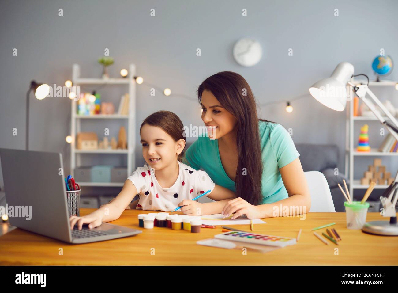 Online-Training für Kinder. Mutter und Tochter beim Betrachten von Videostunden Zeichenvortrag mit einem Computer im Wohnzimmer. Stockfoto