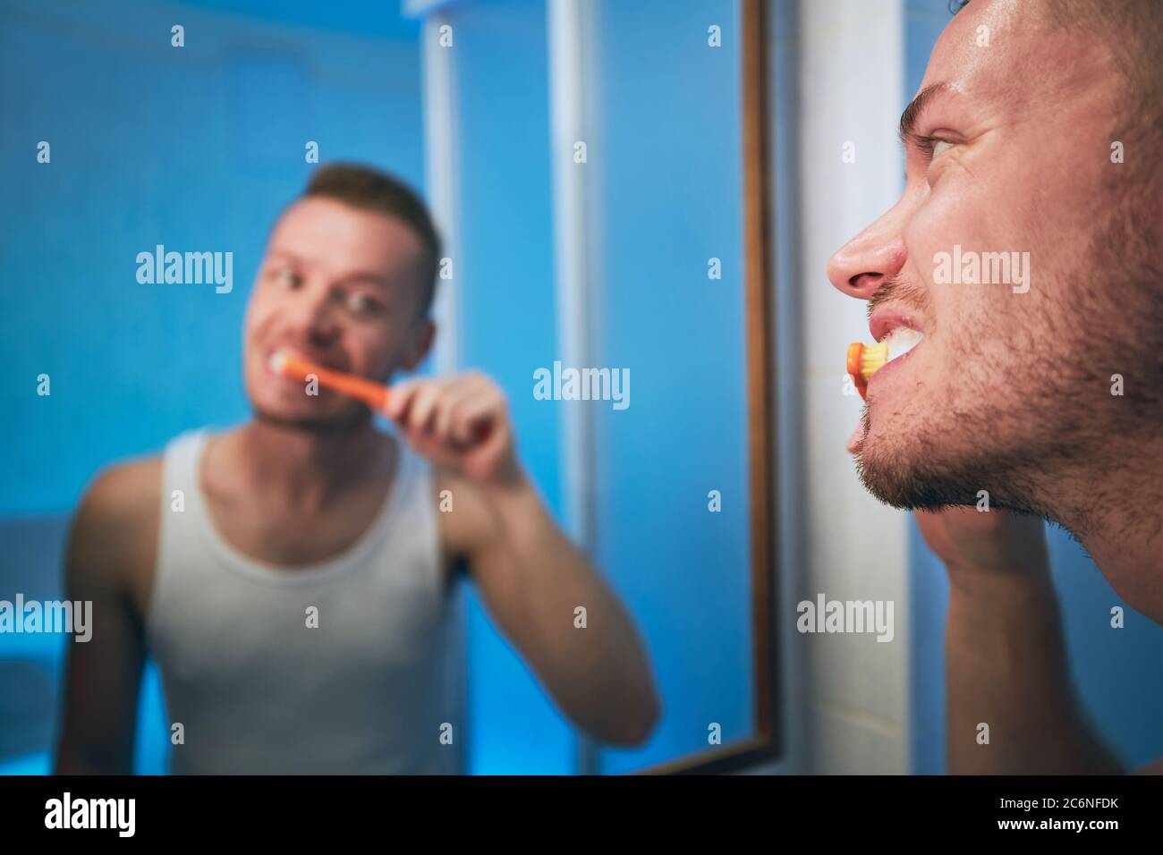 Morgendliche Hygiene. Mann putzt Zähne und sieht in den Spiegel des eigenen Badezimmers. Stockfoto