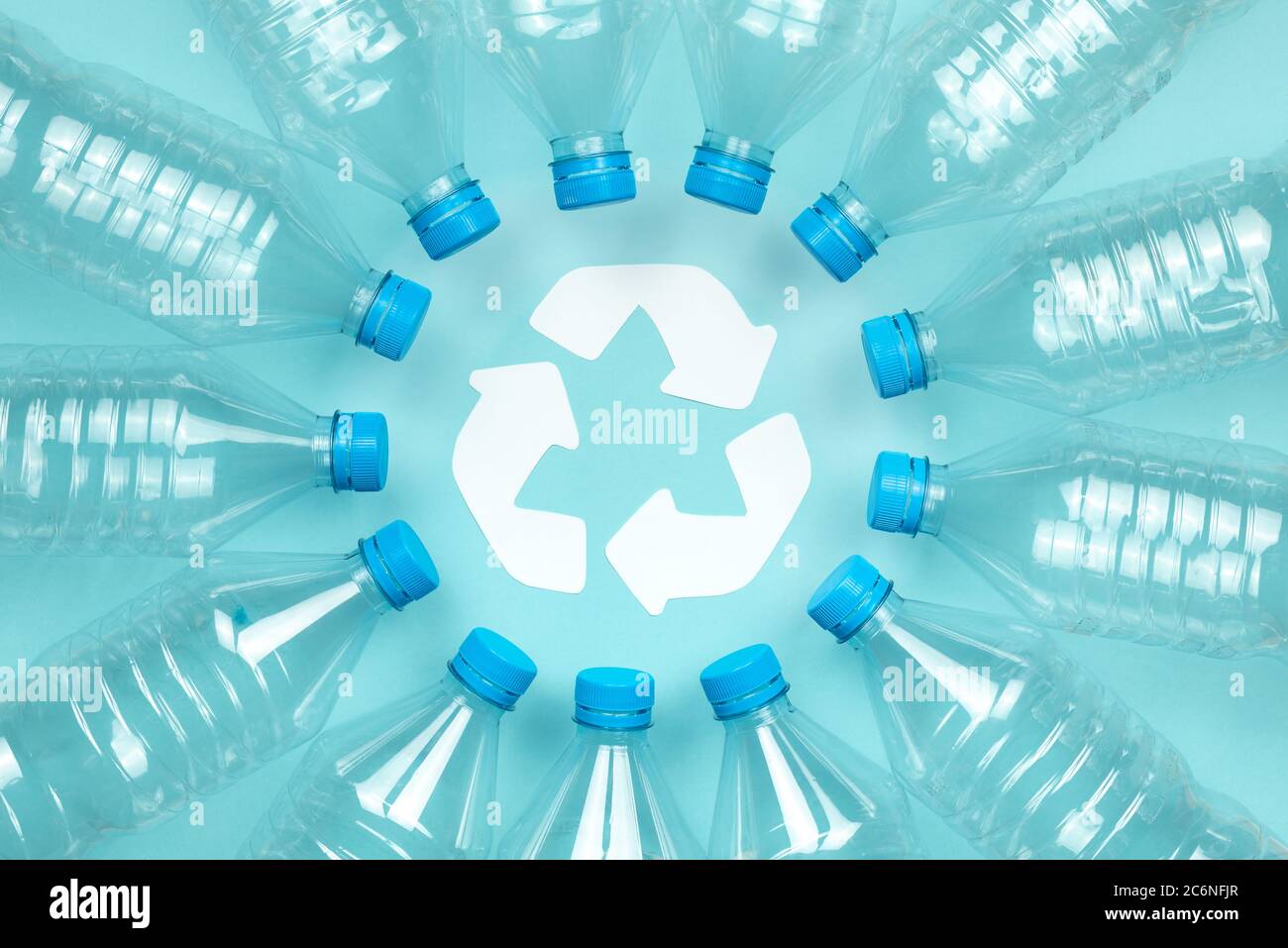 Horizontales Farbbild mit einer Überkopfansicht einer durchsichtigen Kunststoffflasche mit Verschlüssen auf blauem Hintergrund. Recycling- und Umweltkonzept. Stockfoto