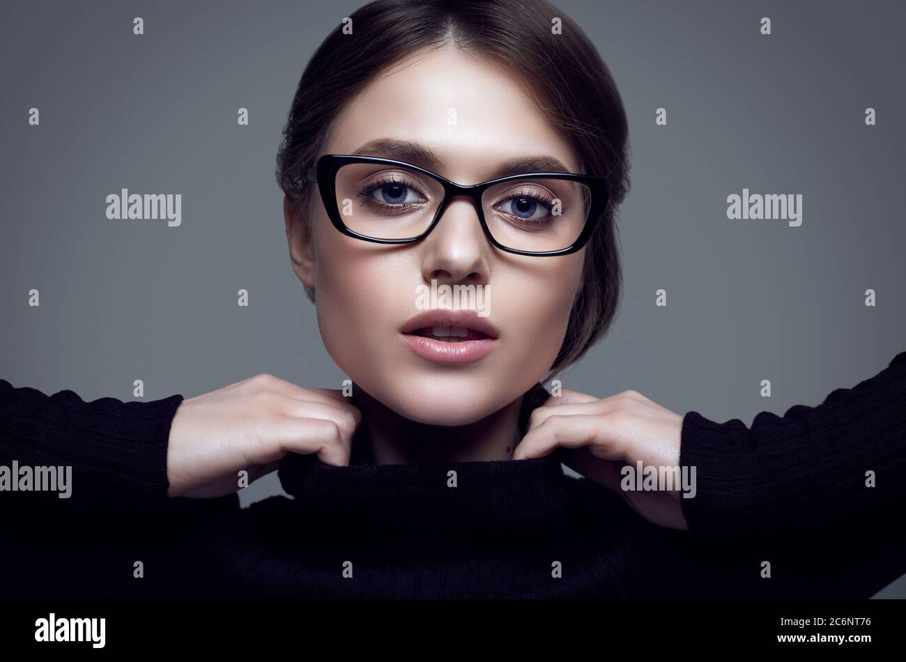 Portrait von niedlichen Student Mädchen trägt schwarzen Rollkragen Pullover und stilvolle Brillen posiert auf grauem Hintergrund im Studio Stockfoto