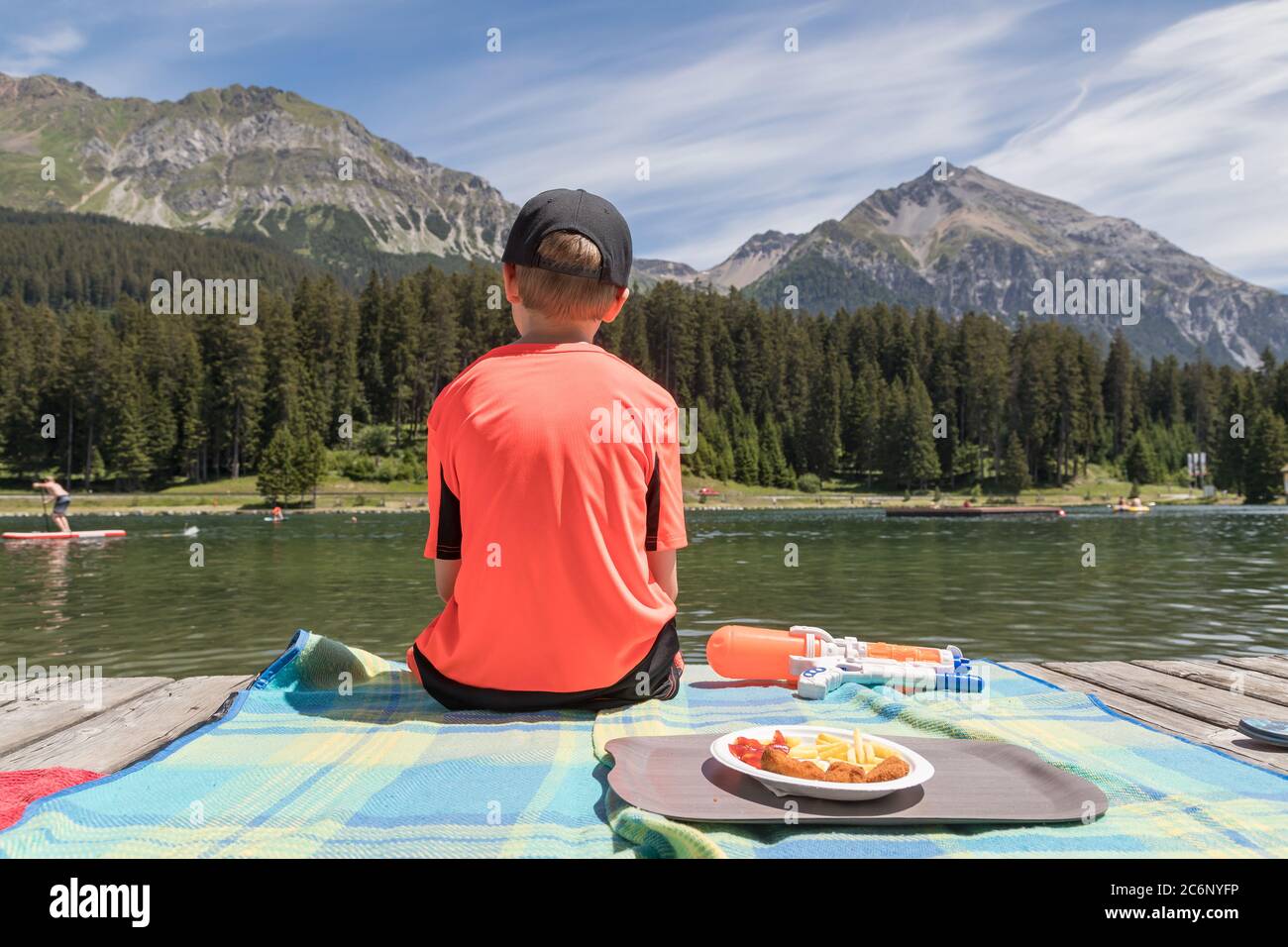 Junge sitzt auf einer Holzpromenade und schaut auf einen See Stockfoto