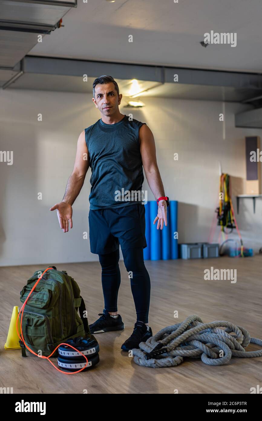 Motivierter Boot Camp Trainer steht mit Fitnessgeräten in der Turnhalle. Hanteln, Seil, Sandsack auf Holzboden. Porträt des libanesischen Sportlehrers. Stockfoto