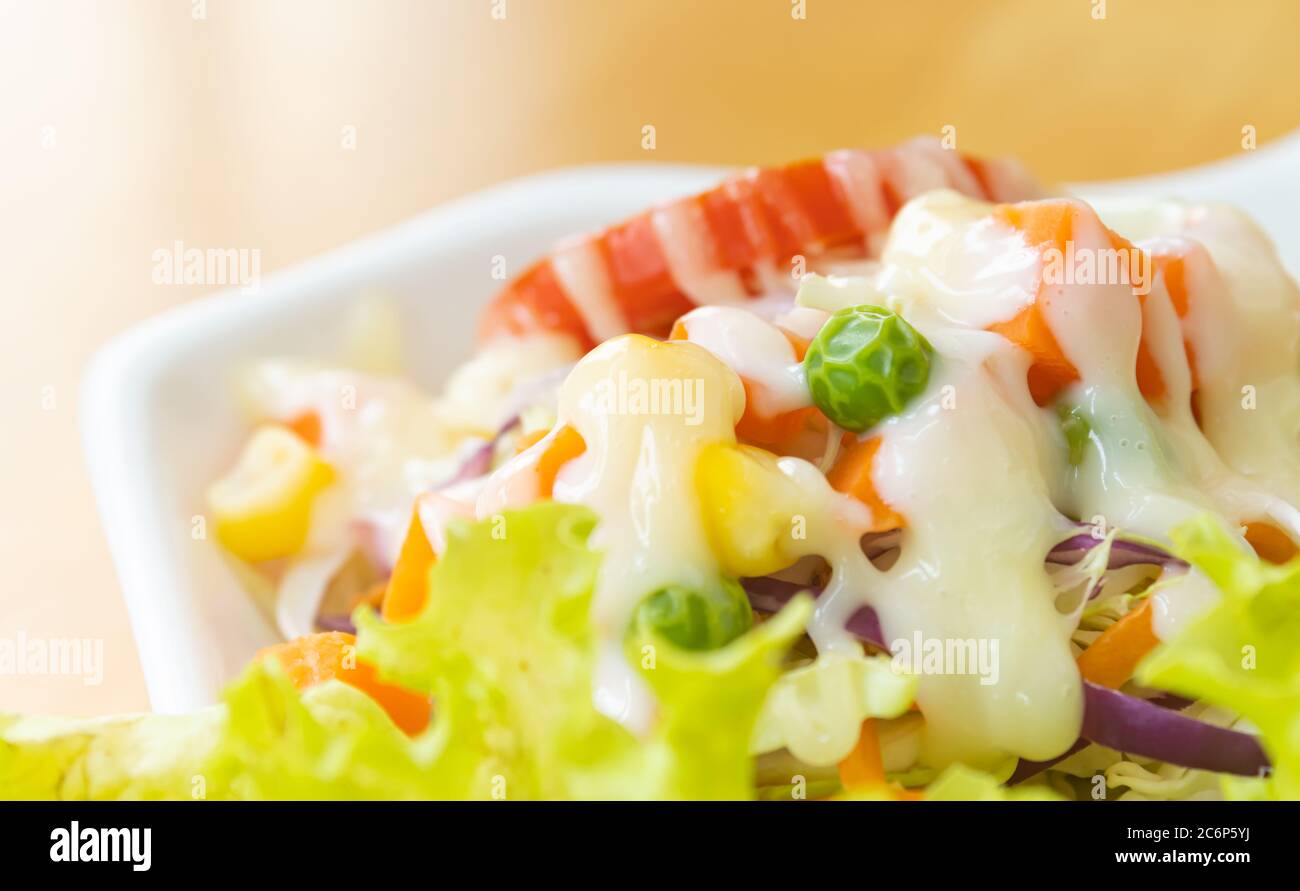 Veganer Salat oder Vegetarischer Salat sind Erbsen und Mais und Tomaten und Karotten und Kohl und Salat mit Mayonnaise auf Holztisch am Seitenrahmen mit N Stockfoto