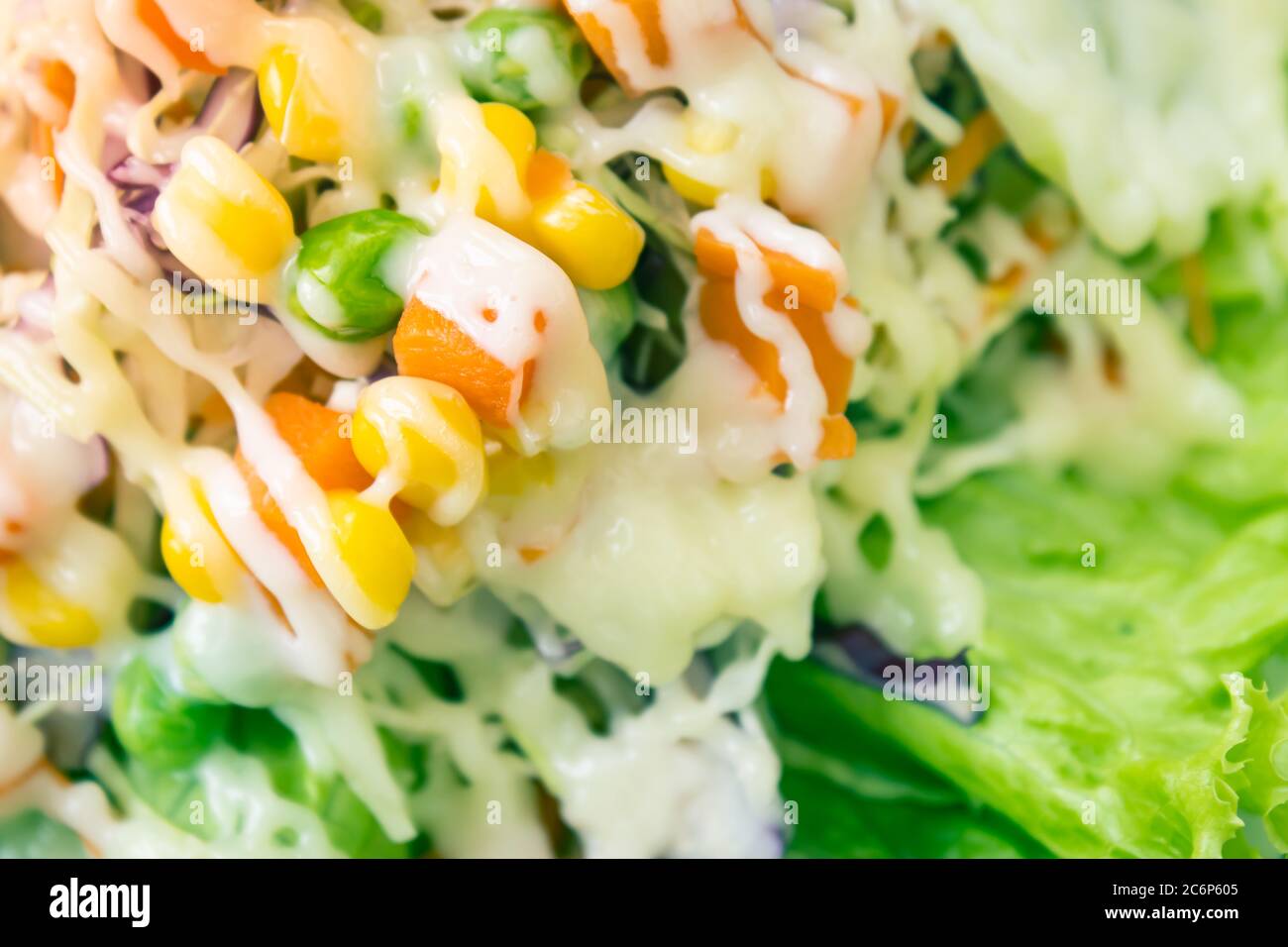 Veganer oder vegetarischer Salat mit Mayonnaise Topping auf dem linken Rahmen umfasst Karotten und Tomaten und Mais und Kohl sowie Erbsen und Salat in Vintage-Ton Stockfoto