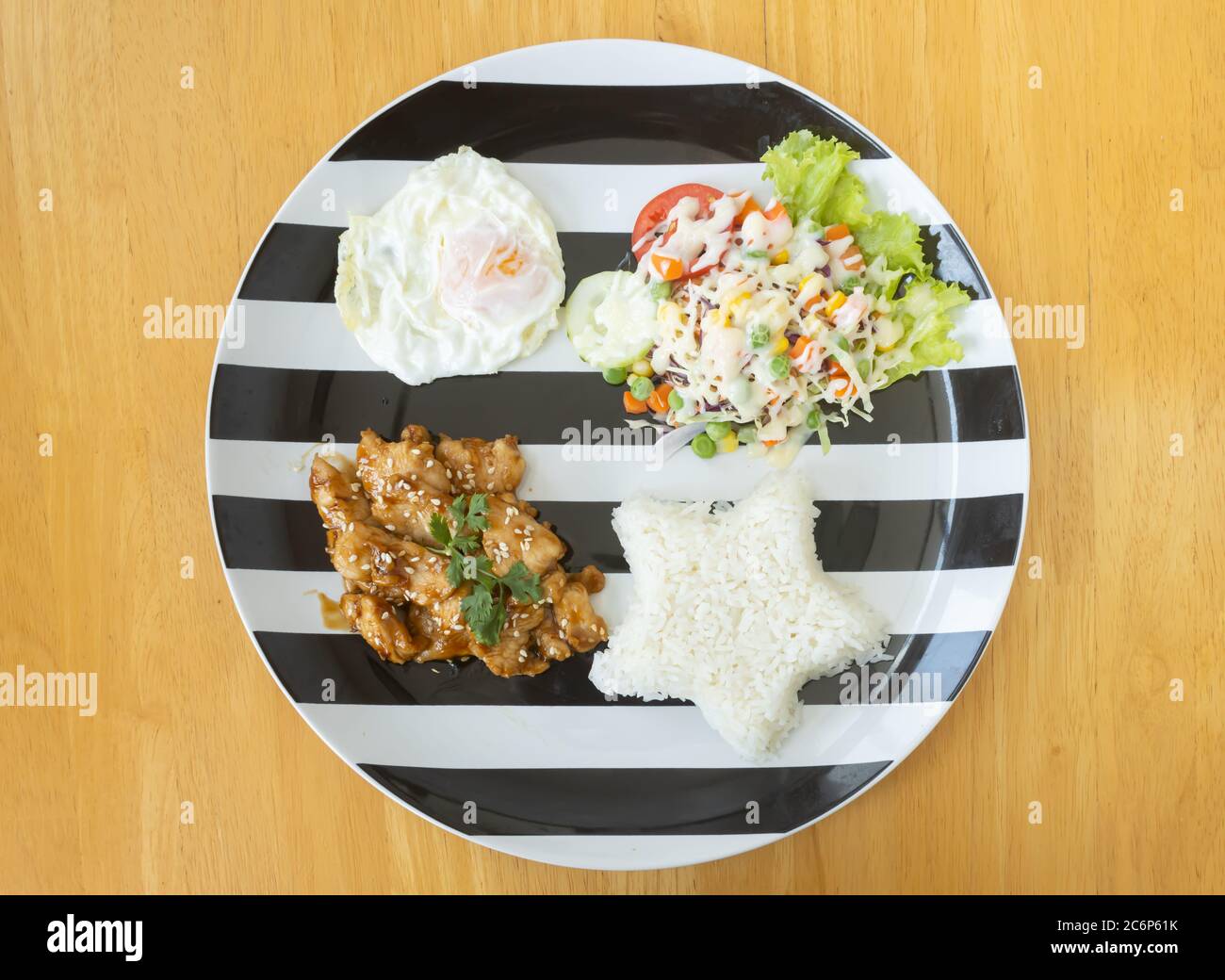 Gebratenes Huhn mit Knoblauch und Pfeffer und gebratenes Ei und Veganer Salat und Reis in Schale auf Holztisch mit natürlichem Licht auf Flatlay View Stockfoto