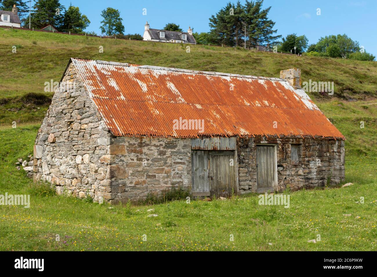 TALMINE UND TALMINE BAY SUTHERLAND SCHOTTLAND SOMMER DIE ALTE STEINHÜTTE MIT ROSTIGEN ROTEN WELLBLECHDACH IN DER NÄHE DES STRANDES Stockfoto