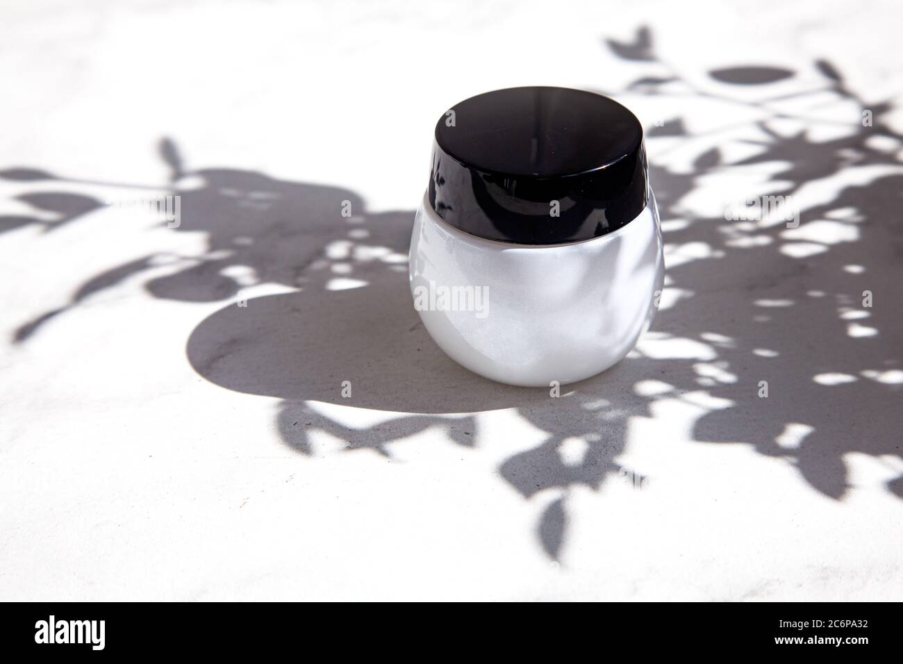 Ein schönes weißes Glas Creme auf dem Marmorboden im Schatten der Blätter von der hellen Sonne. Sommer Zusammensetzung flach legen Stockfoto