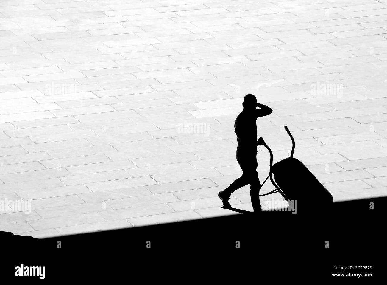 Silhouette eines Mannes, der eine Schubkarre auf dem Bürgersteig leert, in kontrastreicher Schwarz-Weiß-Ansicht mit hohem Winkel Stockfoto