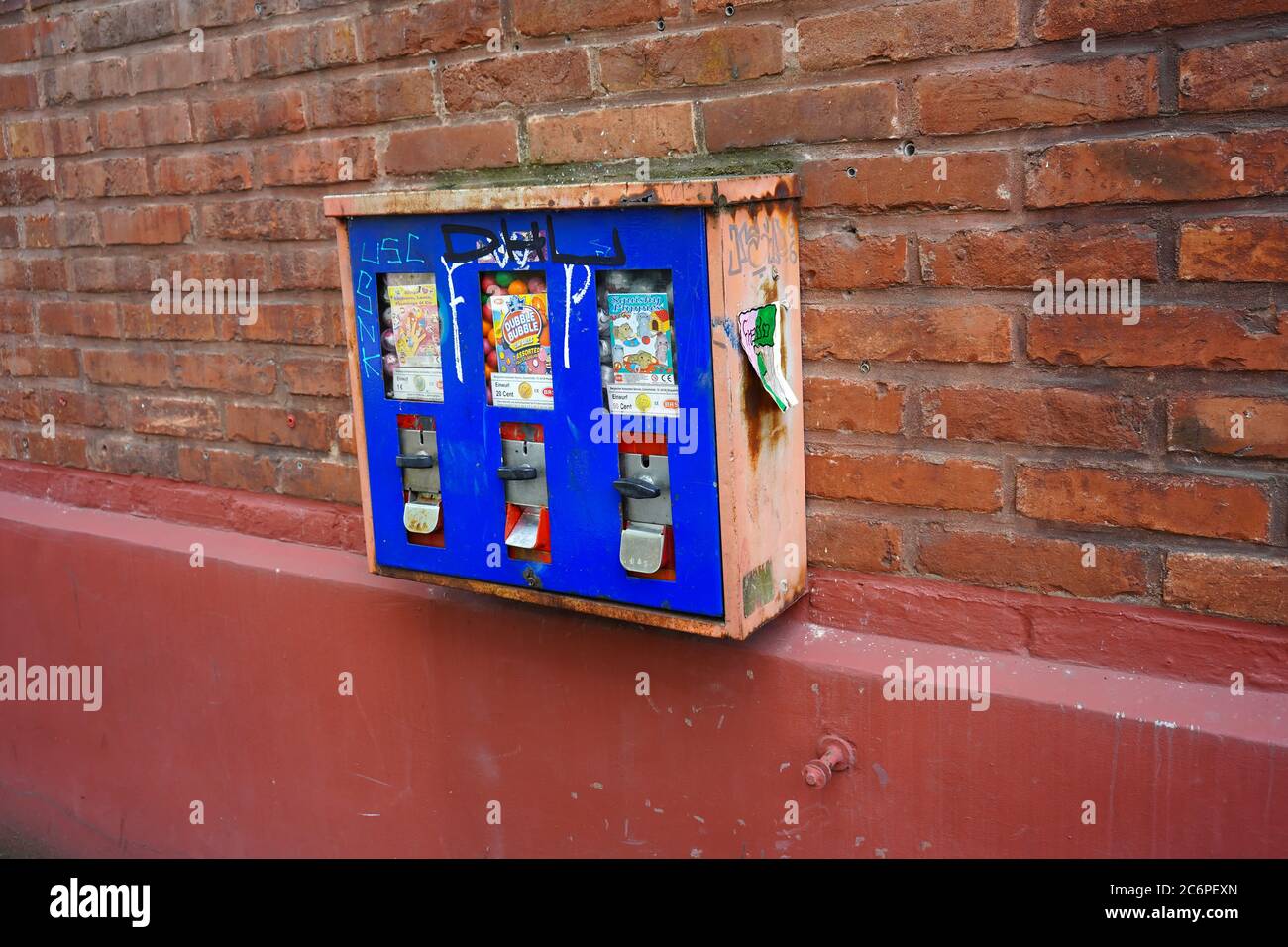 Seitenansicht eines Vintage-Kaugummi-Münzautomaten an der Wand eines Gebäudes in Deutschland. Stockfoto