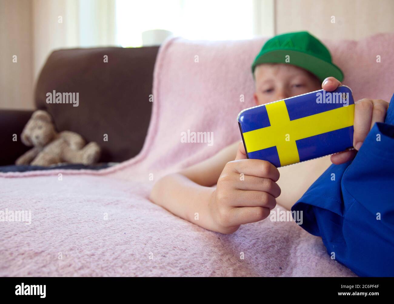Ein kleiner Kerl, der mit seinem Handy im Internet surft, mit einer Handyhülle in Form der schwedischen Flagge. Foto Jeppe Gustafsson Stockfoto