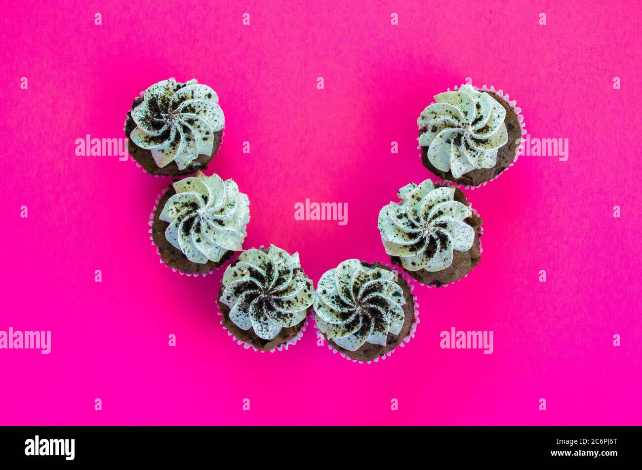 6 Kekse und Cupcakes in einem Halbkreis von oben auf einem hellen rosa Hintergrund betrachtet Stockfoto