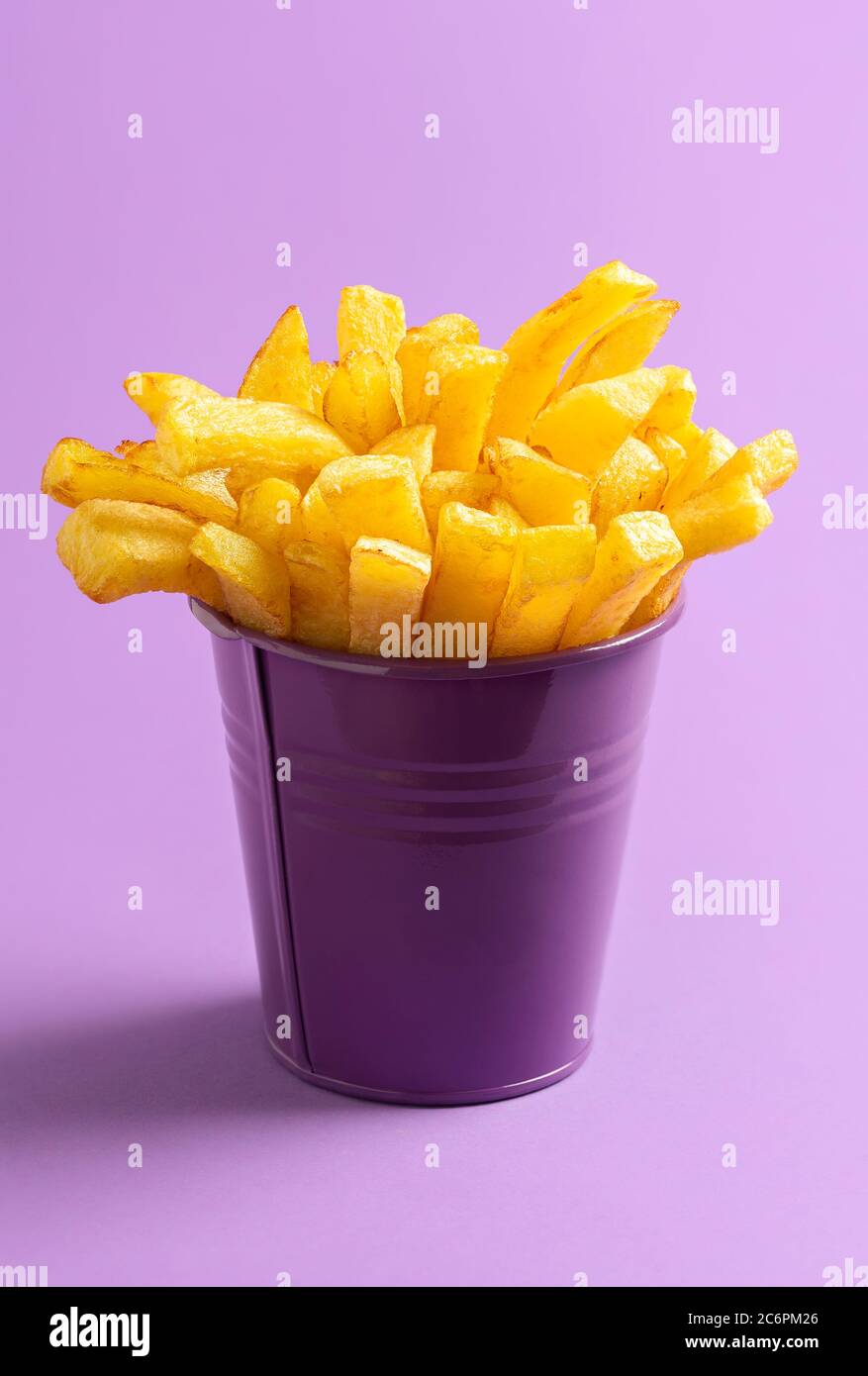 Eimer Pommes frites isoliert auf lila nahtlosen Hintergrund. Goldene frittierte Kartoffeln in einem lila Eimer. Hausgemachte Fingerchips. Fast Food Rezept Stockfoto