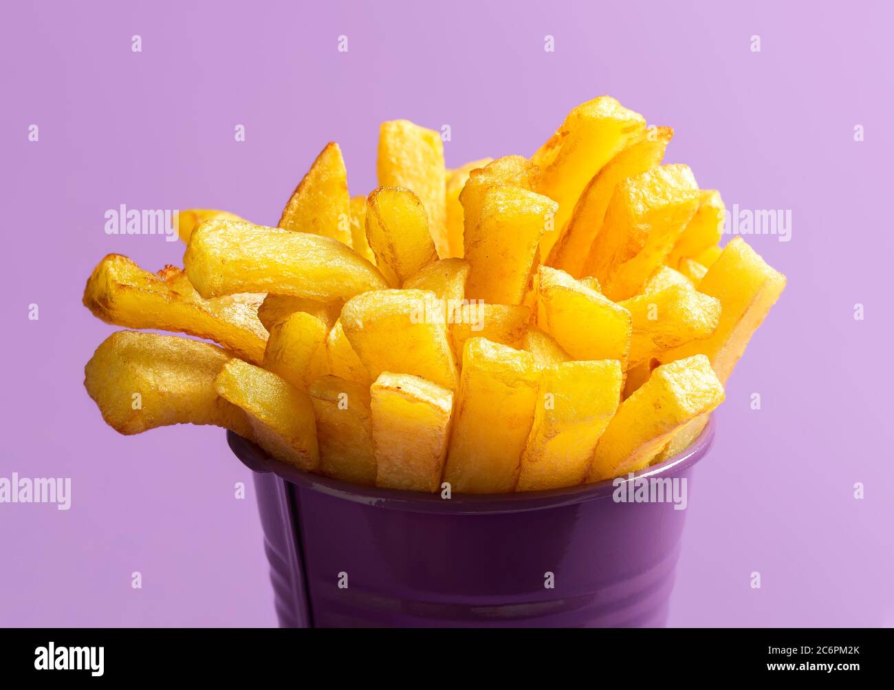 Hausgemachte pommes Frites aus der Nähe, isoliert auf violettem Hintergrund. Frittierte Kartoffeln, Fingerchips, Makrobild. Goldene pommes in einem lila Eimer Stockfoto