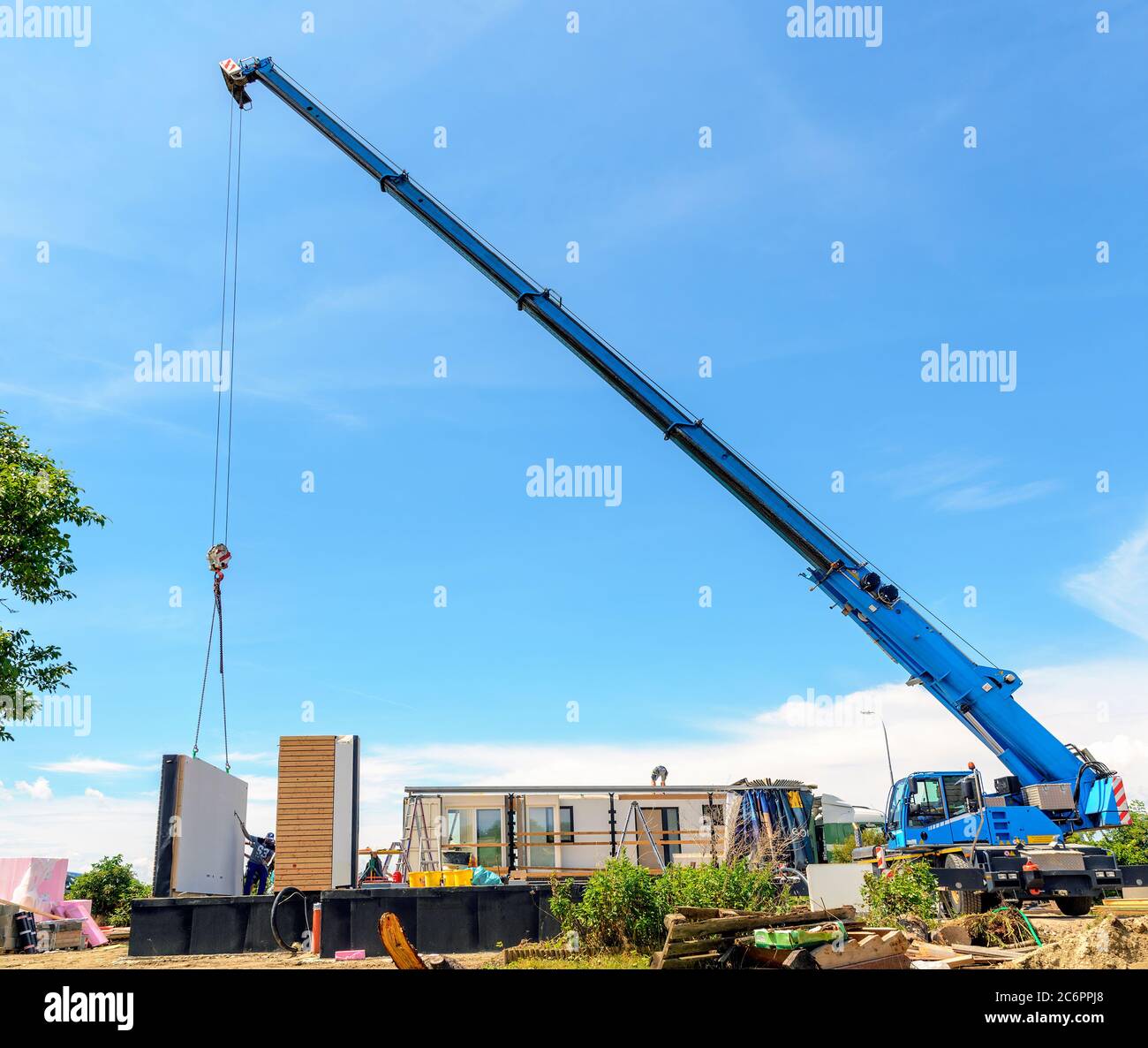 Mobilkran auf einer Baustelle hebt eine Wand eines Fertighauses auf das Fundament Stockfoto