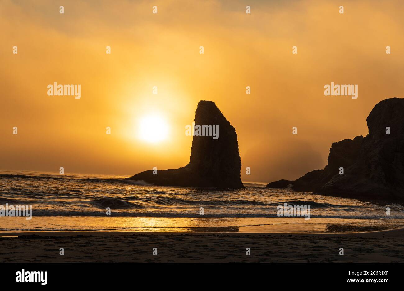 Orangefarbener Sonnenuntergang erhellt den Himmel und Silhouetten, die das Meer entlang Bandon Beach in Oregon stapelt Stockfoto