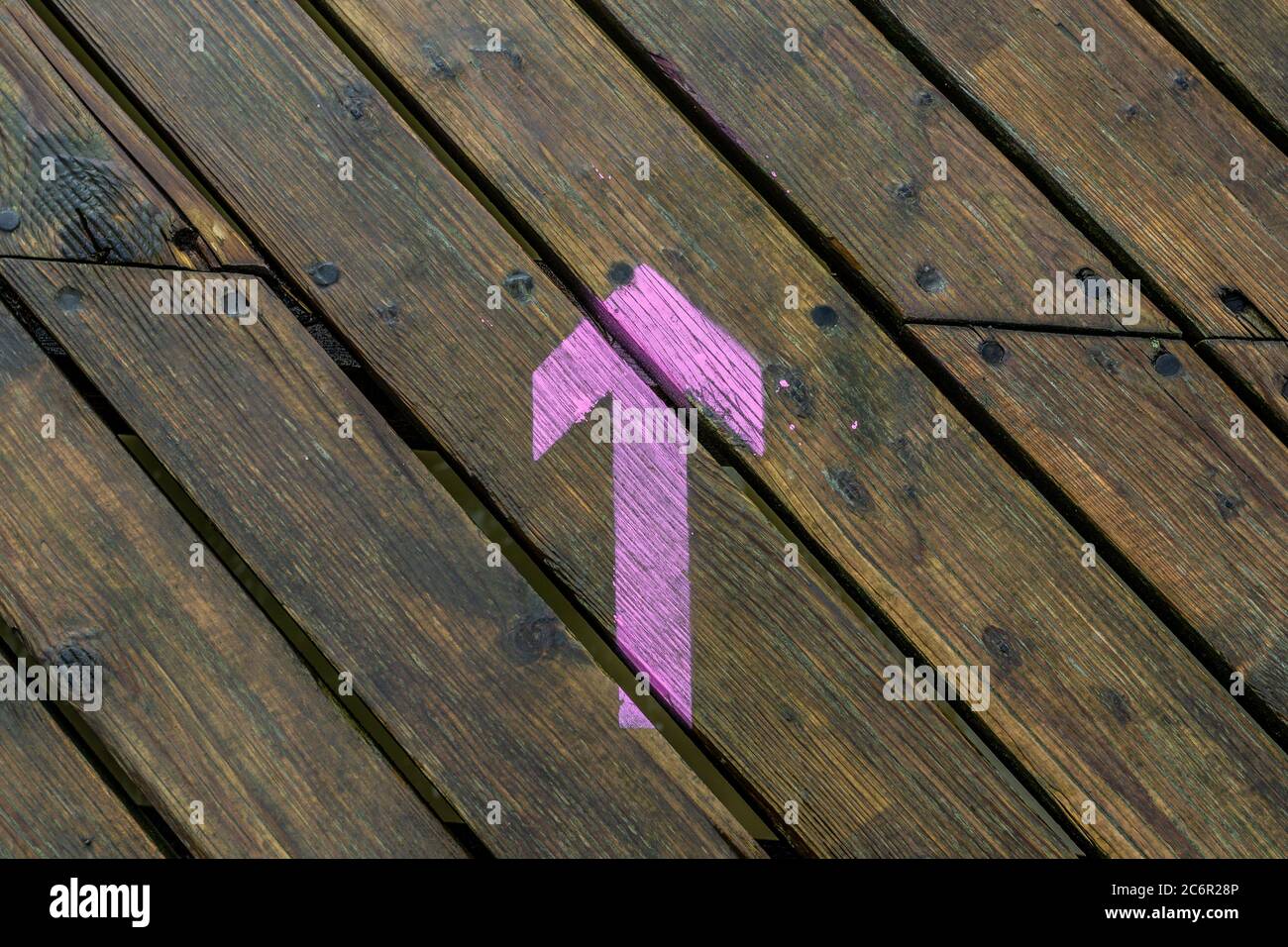 Ein rosa gemalter vorwärts zeigender Pfeil auf hölzerner diagonaler Terrasse, Pfeil nach vorne zeigend Stockfoto