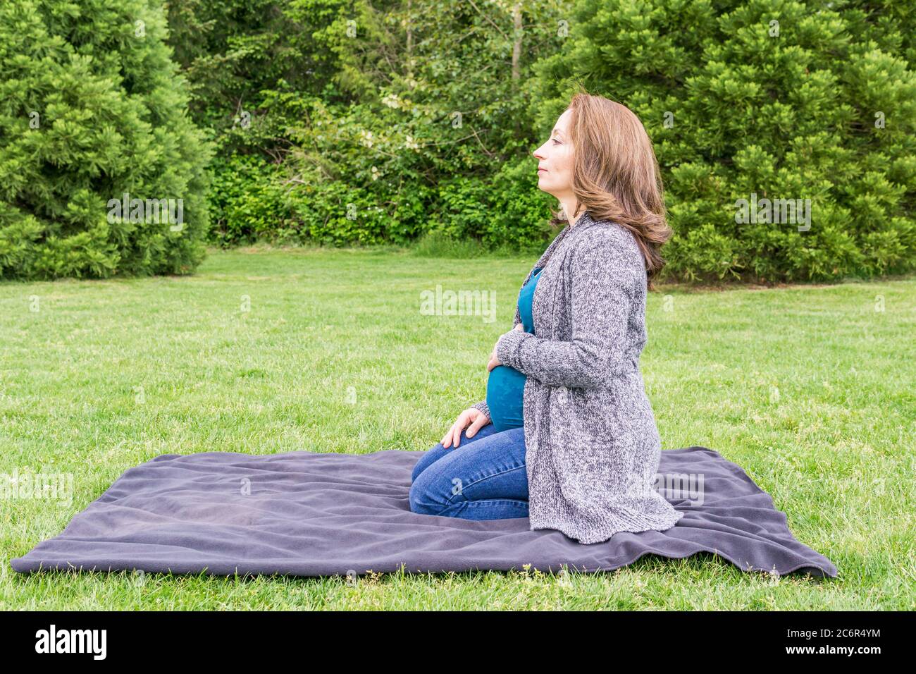 Glücklich schwangere kaukasische Frau entspannen in einem Park mit den Händen auf ihrem Bauch. Stockfoto