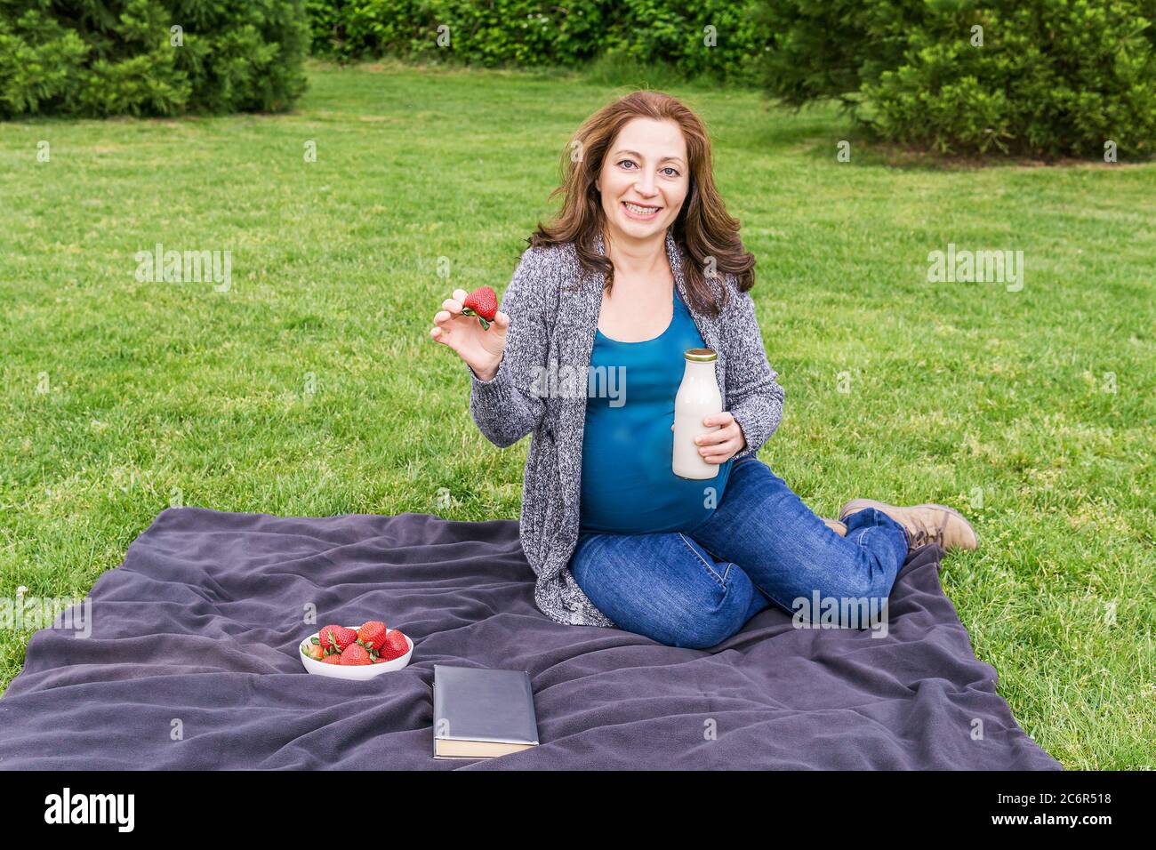 Schwangere Frau mit einer Flasche Milch auf einem grünen Feld in einem Park. Stockfoto