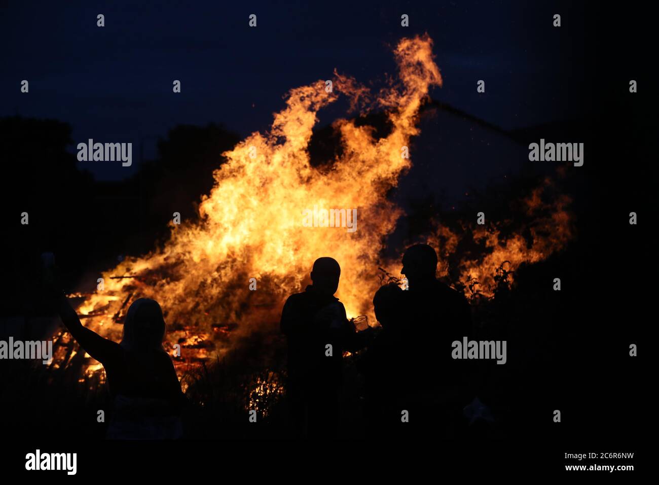 Die Menschen beobachten ein Lagerfeuer auf der Shankill Road in Belfast, während um Mitternacht Lagerfeuer entzündet werden sollten, als Teil einer loyalistischen Tradition, um den Jahrestag des Sieges des protestantischen Königs Wilhelm gegen den katholischen König James in der Schlacht von Boyne im Jahr 1690 zu begehen. Stockfoto