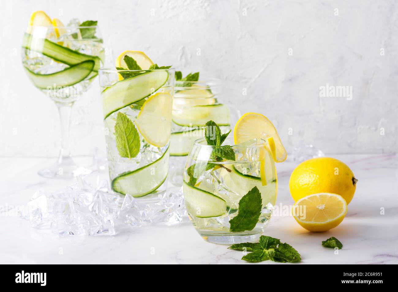 Alkoholgetränk (Gin Tonic Cocktail) in verschiedenen Gläsern mit Zitrone, Gurke, Minzblättern und Eis auf Weiß. Eisgetränk mit Zitrone. Stockfoto