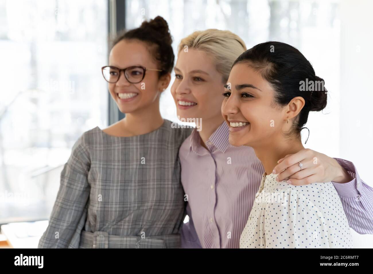 Lächelnde multiethnische weibliche Kollegen umarmen zeigen Einheit bei der Arbeit Stockfoto