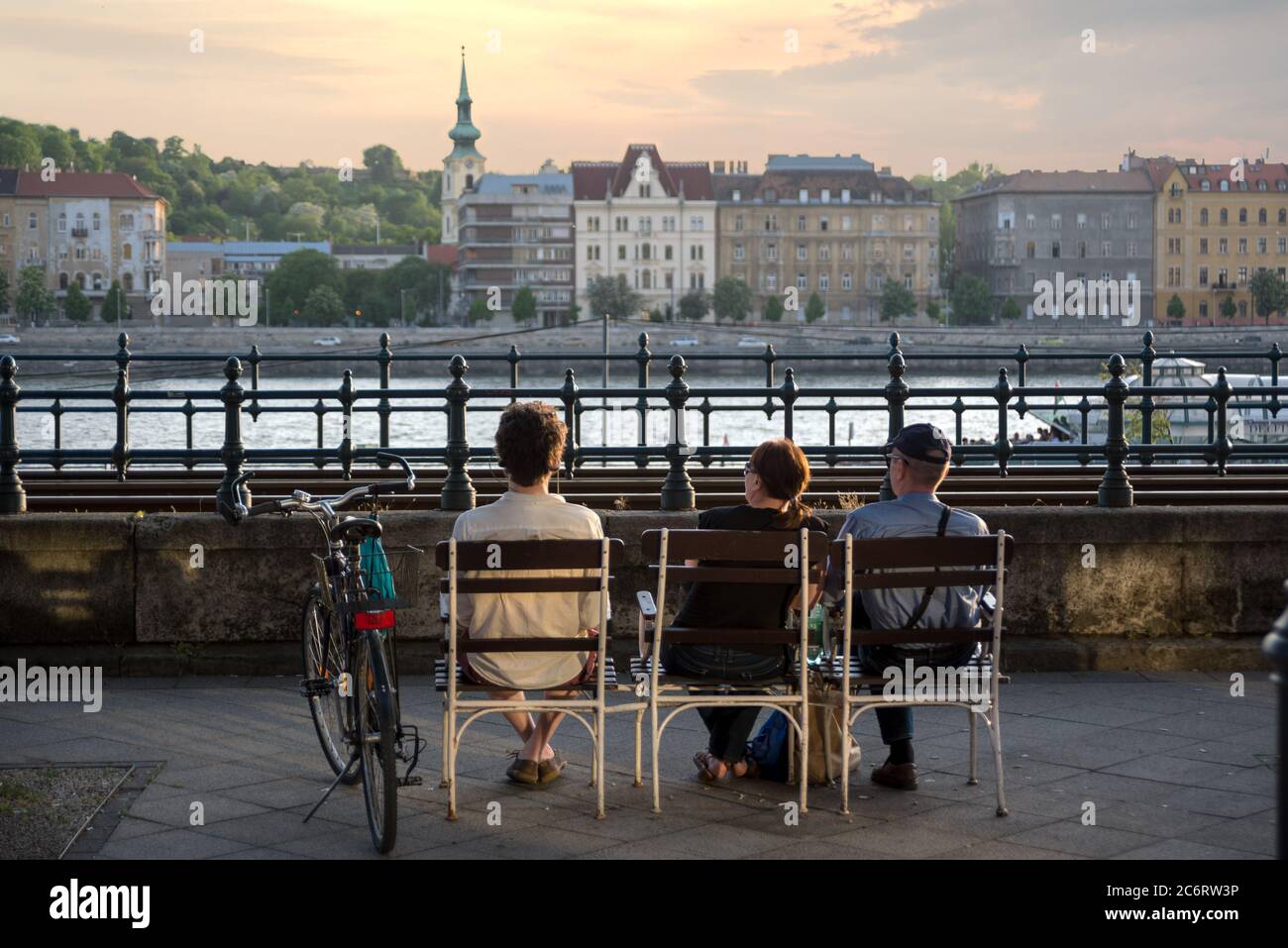 Drei Personen sitzen auf Stühlen an der Donaupromenade genießen Budapest Aussicht. Rückansicht Stockfoto