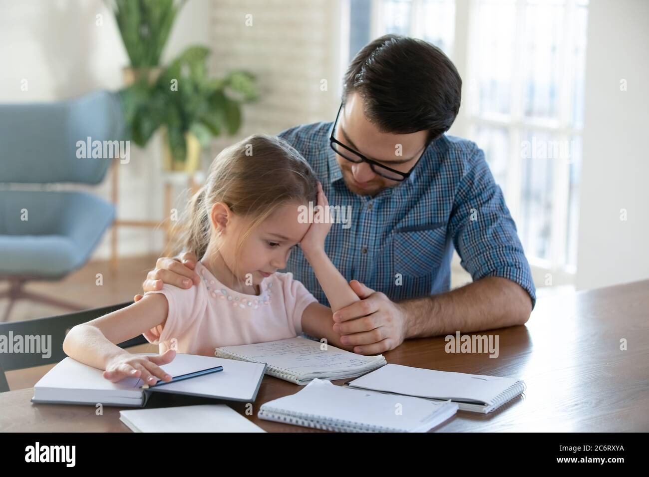 Fürsorglicher Vater hilft verärgert kleine Tochter mit Schulaufgaben Stockfoto