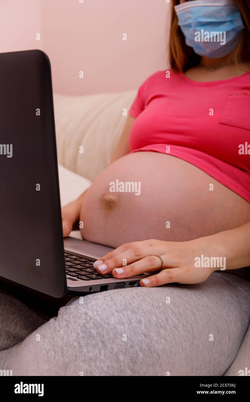 Schwangere Frau mit Bauch mit einem Laptop auf dem Bett. Konzept des Smart Working aufgrund der Quarantäne für covid19 Coronavirus. Bleiben Sie zu Hause im Büro und w Stockfoto