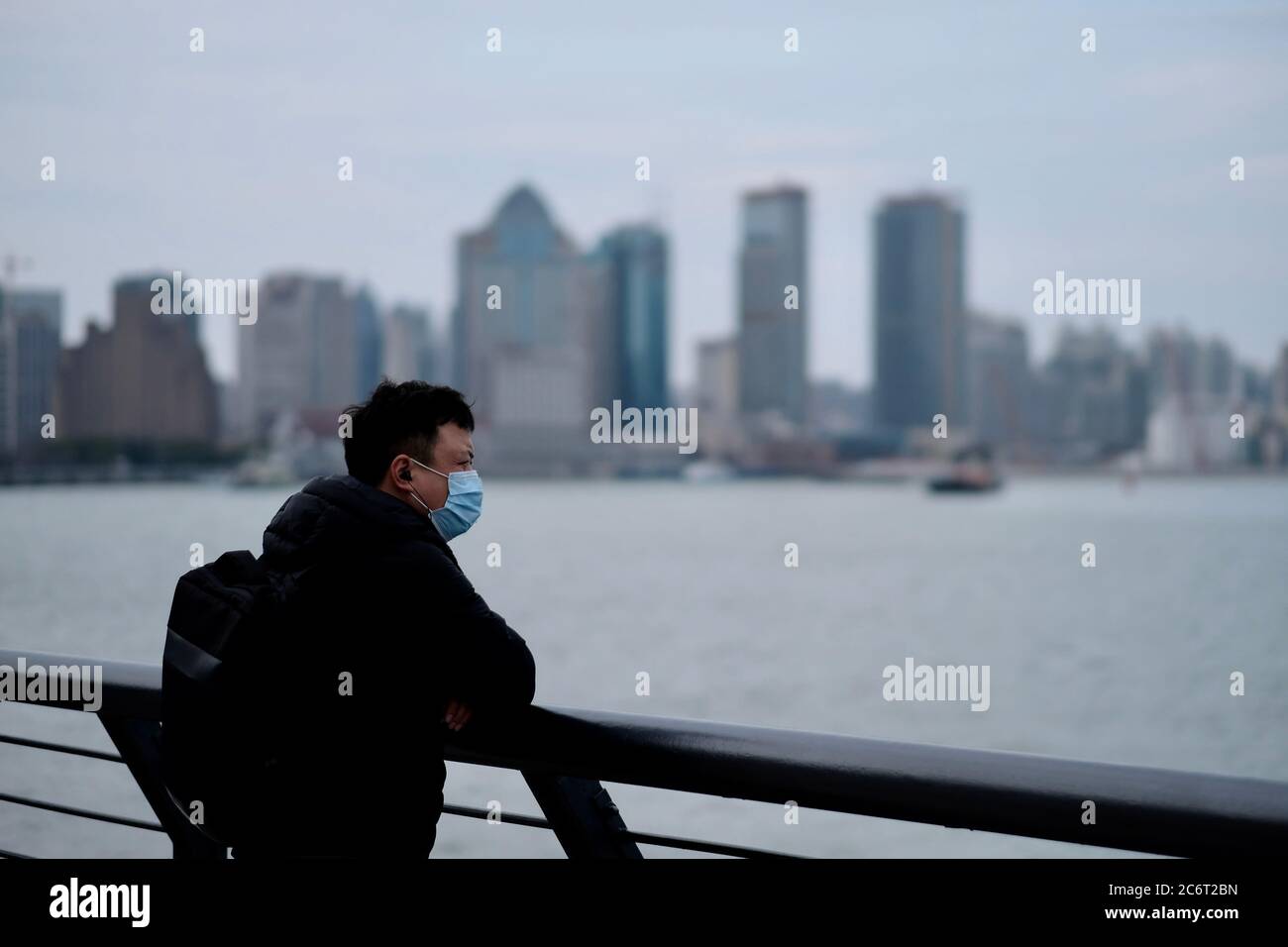 Ein Mann mit einer OP-Maske, der sich auf der Balustrade im bund in China stützt Stockfoto