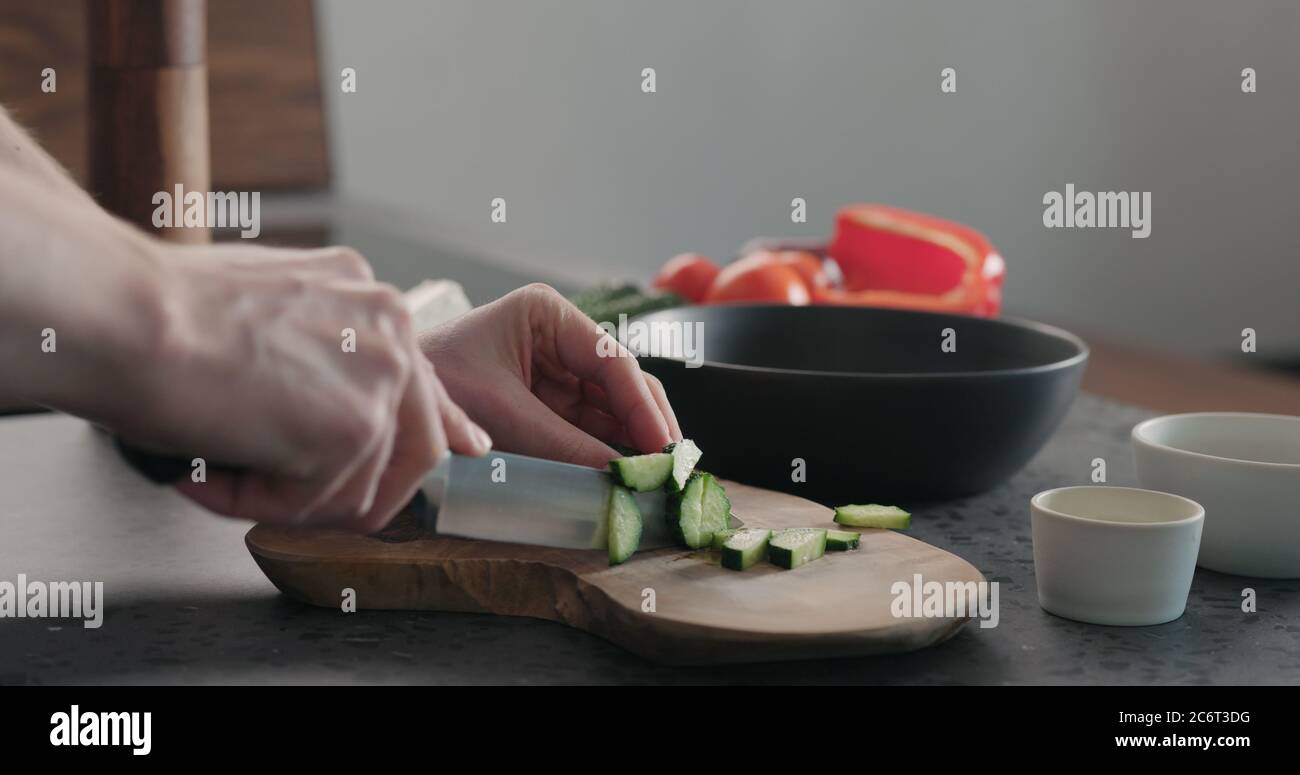 Mann hackt Gurke auf Olivenholz Brett für griechischen Salat Stockfoto