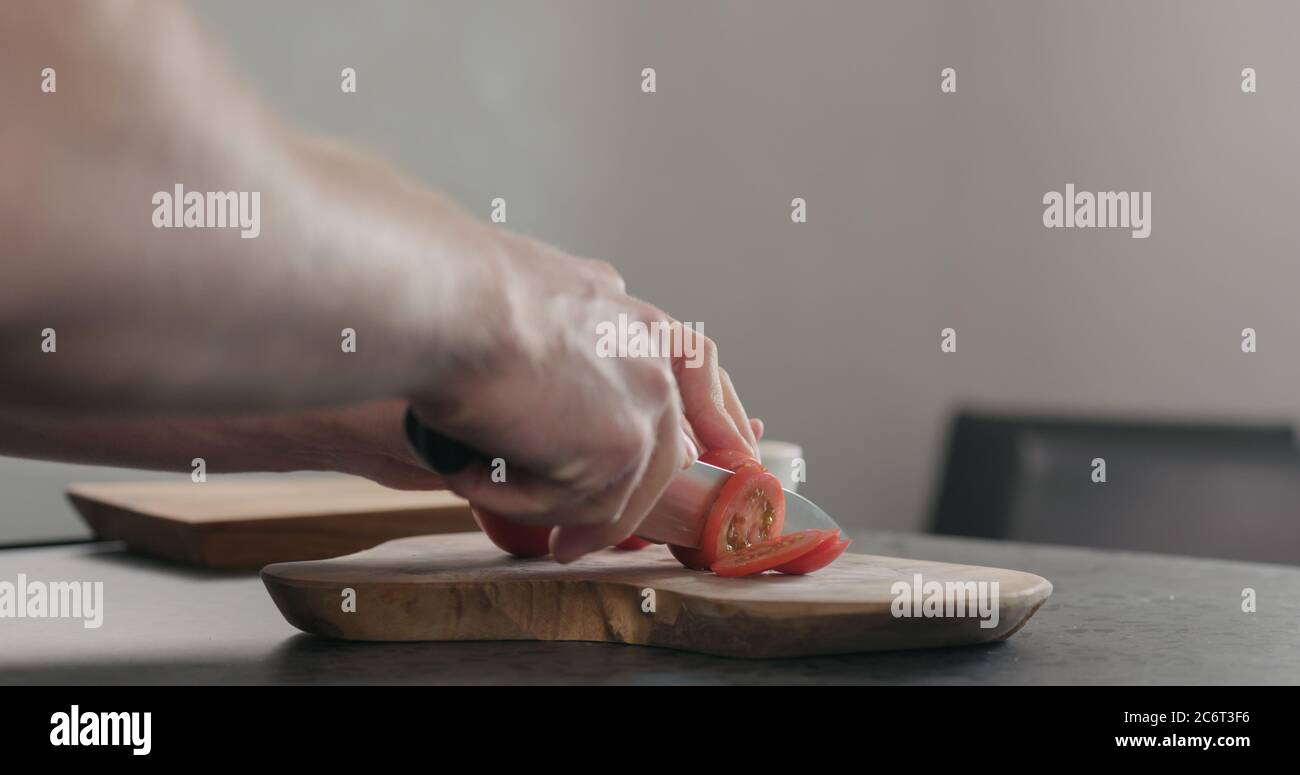 Mann, der Tomaten auf Olivenholz-Brett aufschlitzt Stockfoto