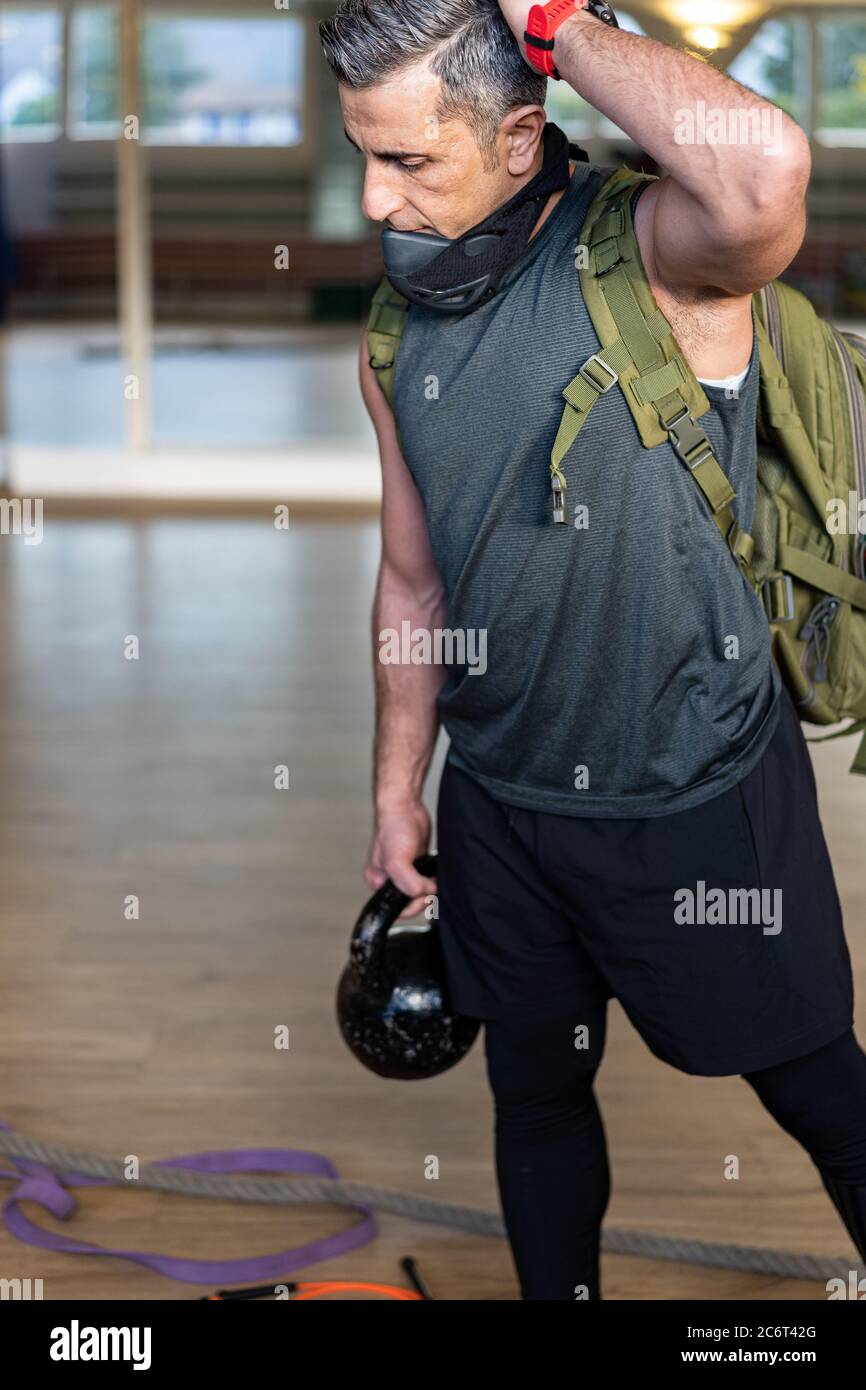 Motivierter Boot Camp Trainer steht mit Fitnessgeräten in der Turnhalle. Tragen Sie Trainingsmaske, Hanteln und Sandsack, Seil und Gummiband auf Holzboden Stockfoto