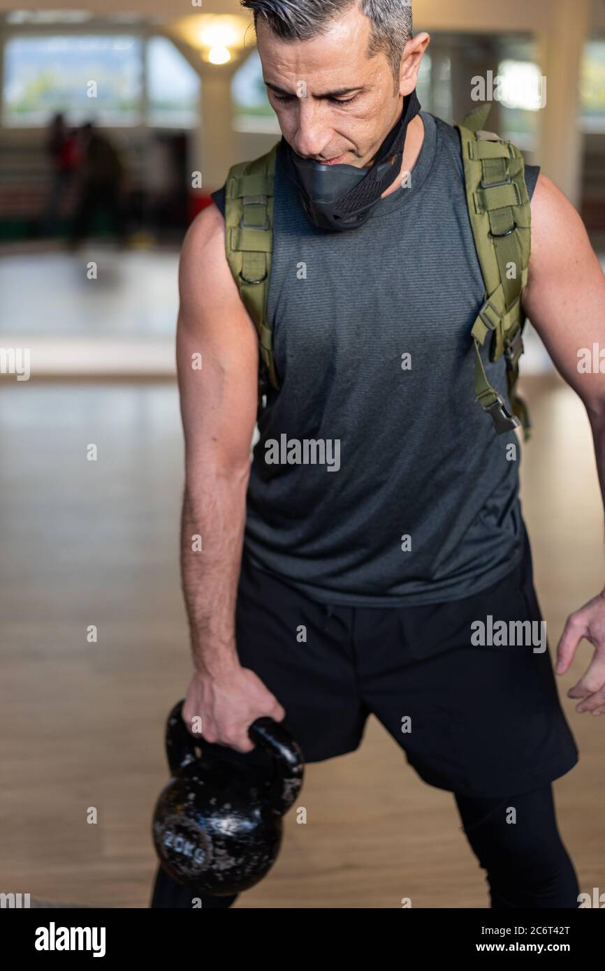 Motivierter Boot Camp Trainer steht mit Fitnessgeräten in der Turnhalle. Tragen Sie Trainingsmaske, Hanteln und Sandsack, Seil und Gummiband auf Holzboden Stockfoto