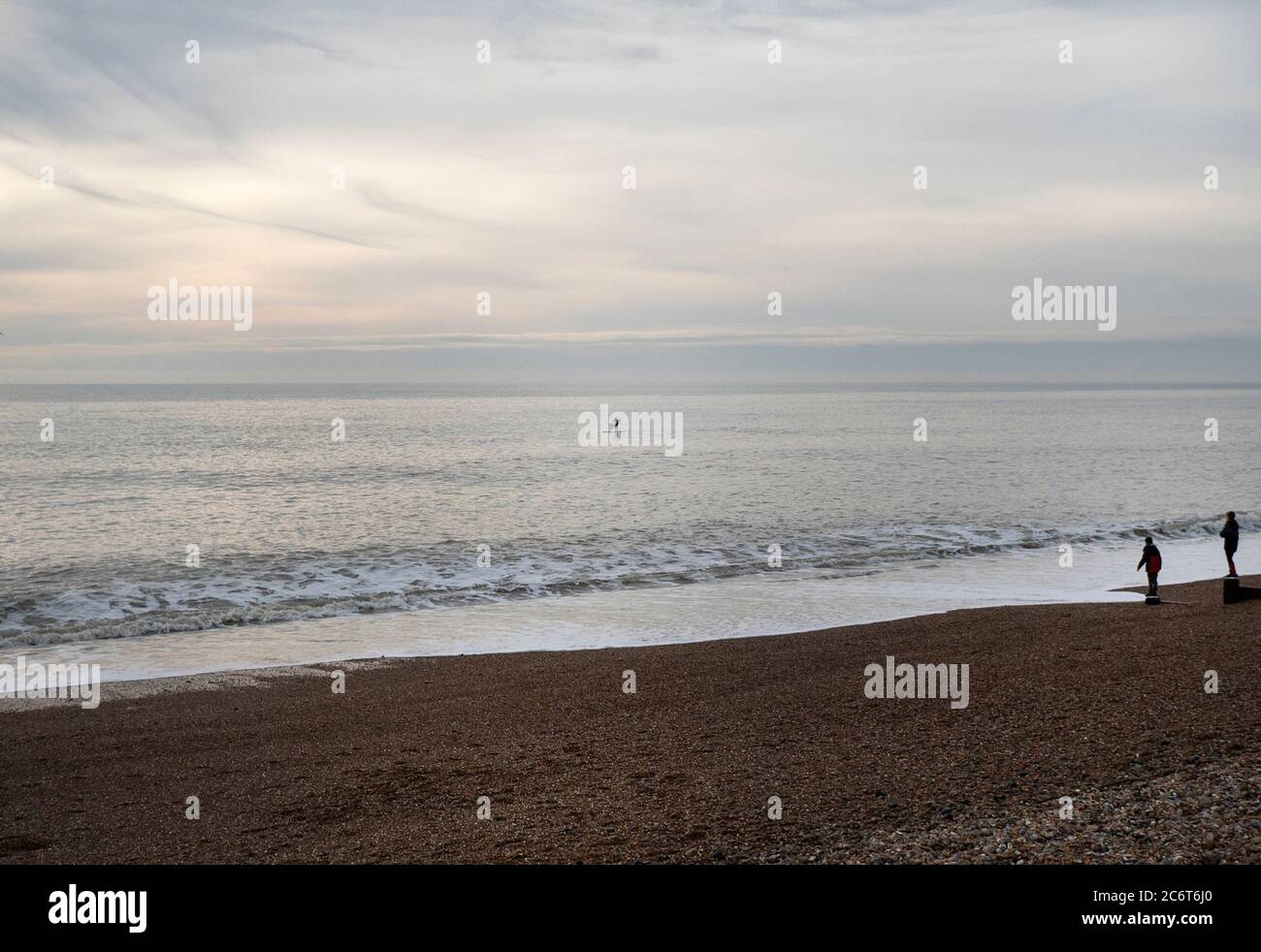 Zwei Leute beobachten EINEN Paddlebarder im frühen Abendlicht vor der Küste in Brighton, East Sussex, Großbritannien Stockfoto