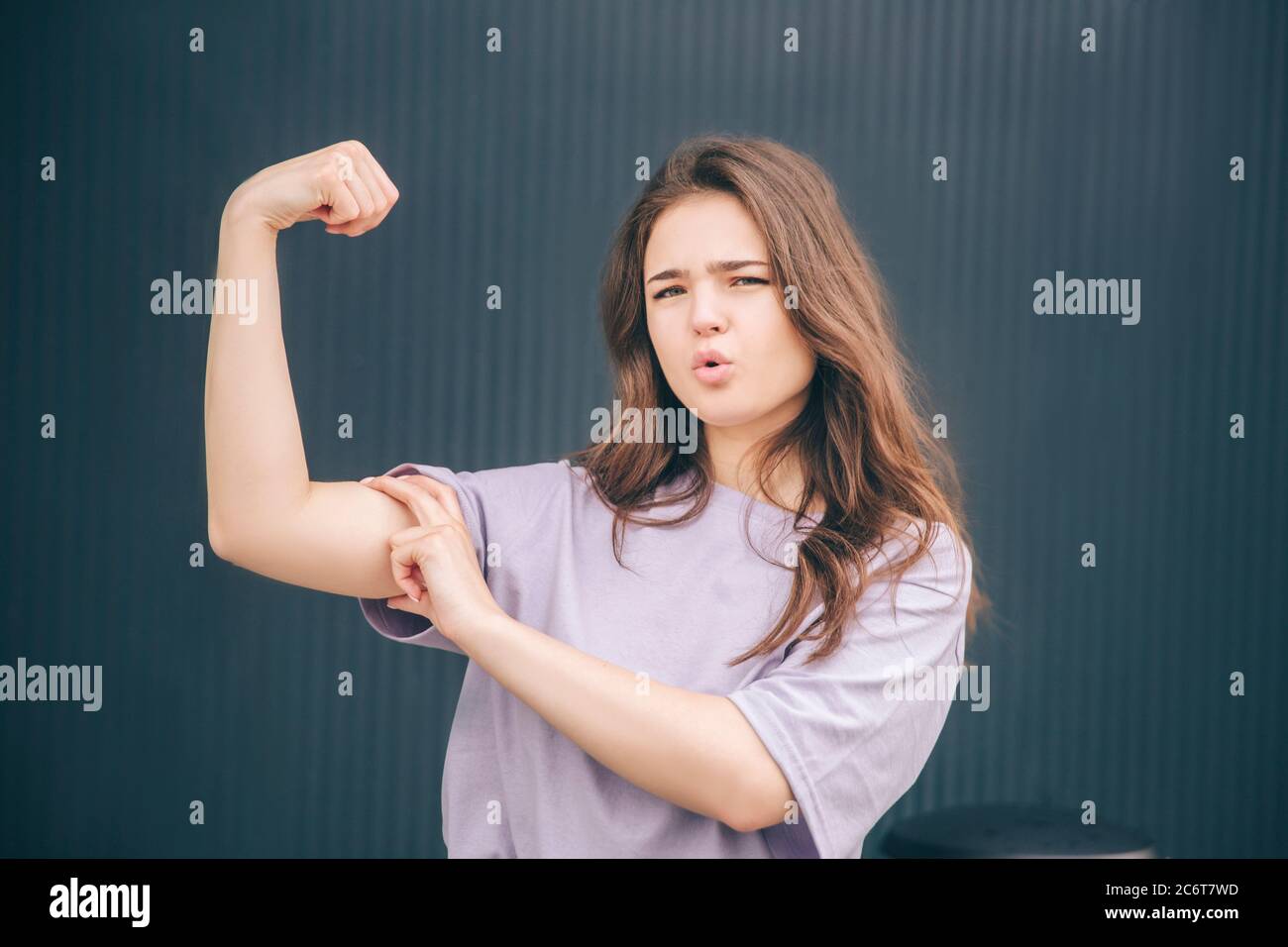 Junge stilvolle trendige Frau isoliert über graublauen Hintergrund. Starke leistungsstarke Mädchen posiert vor der Kamera. Zeigt die Form der Muskeln auf einer Hand. Stand Alone A Stockfoto