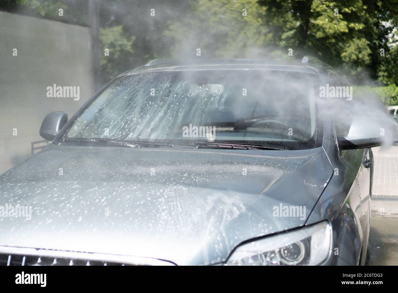 Komplette Autowäsche zur Selbstbedienung. Spritzer Wassertropfen aus einem Spritzgerät, das das Auto spült. Windschutzscheibe. Weißer Schaum Stockfoto