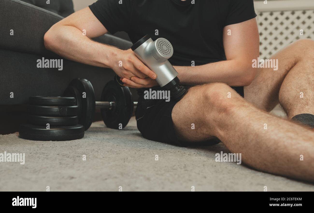 Mann massiert Bein mit Massage Percussion Gerät. Stockfoto