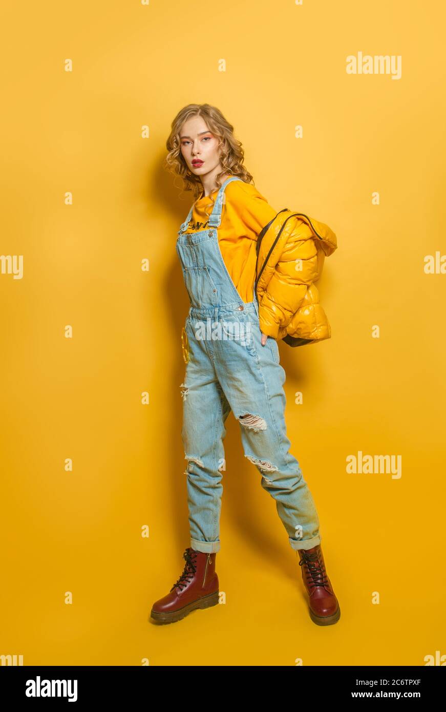 Fashion Frau in Daunenjacke und Jeanssanzug auf hellgelben Hintergrund Stockfoto