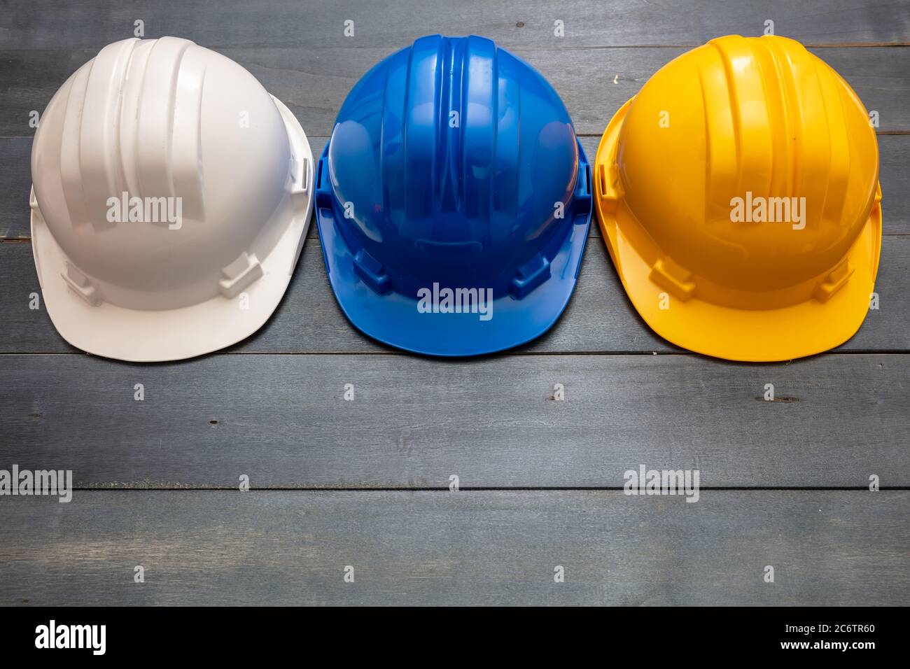 Arbeitsschutzausrüstung. Industrielle Schutzhardhüte weiß, gelb und blau Farben auf Holzgrund. Persönliche Gesundheit und Sicherheit concep Stockfoto