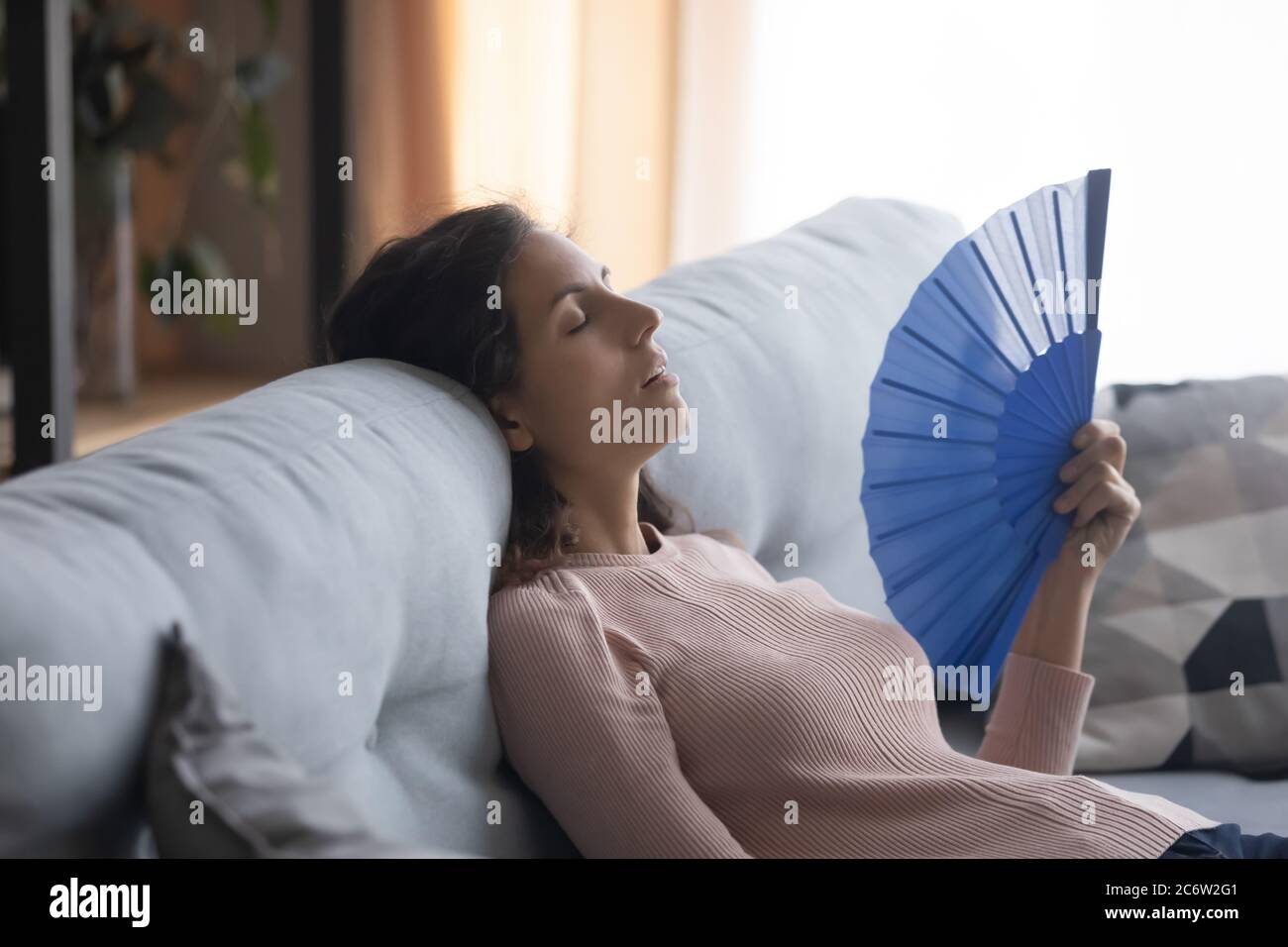 Überhitzte junge Frau winkt mit Handventilator zu Hause Stockfoto
