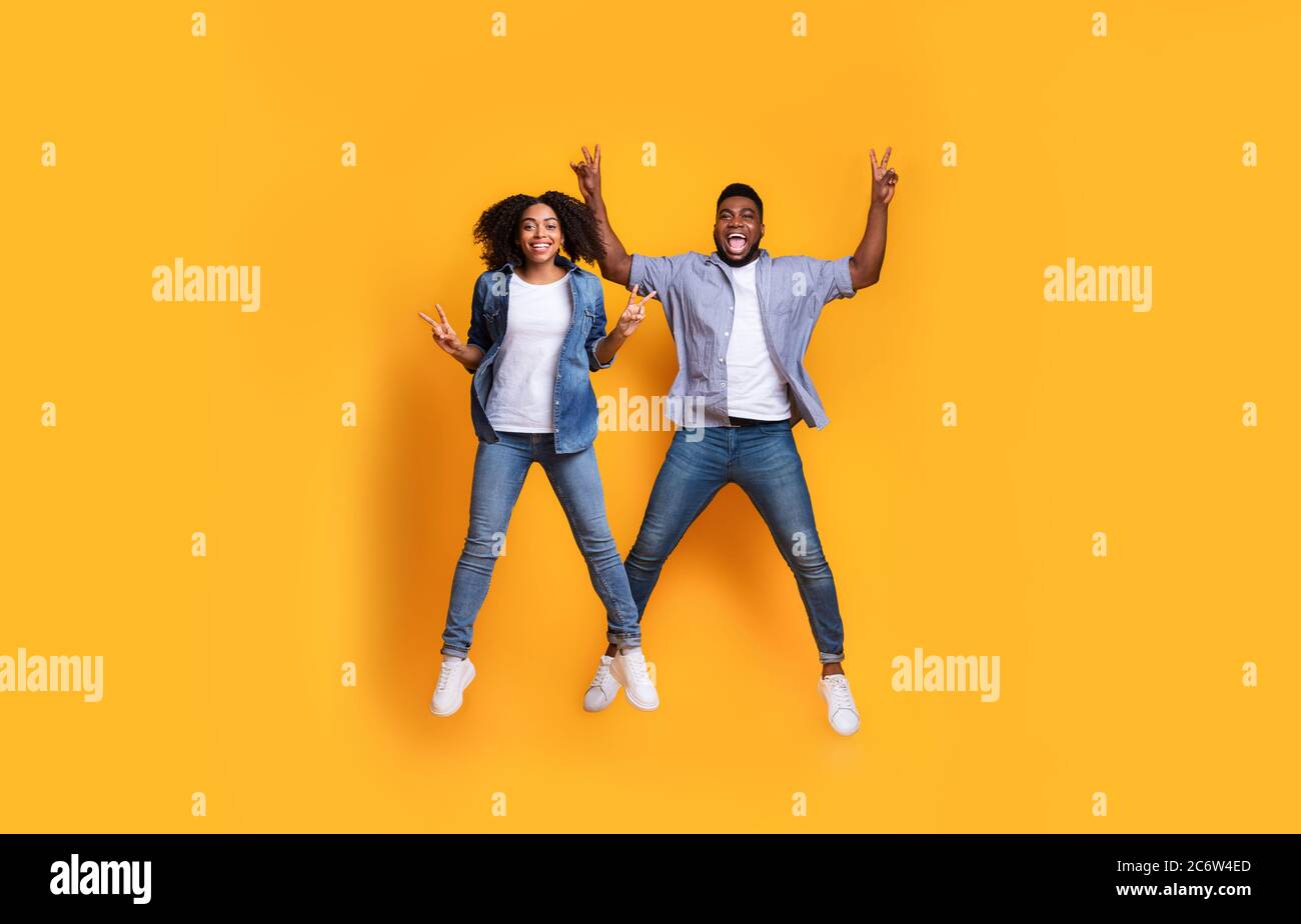 Sorglose Stimmung. Schwarz Kerl Und Mädchen Springen In Luft Und Gesturing Frieden Stockfoto