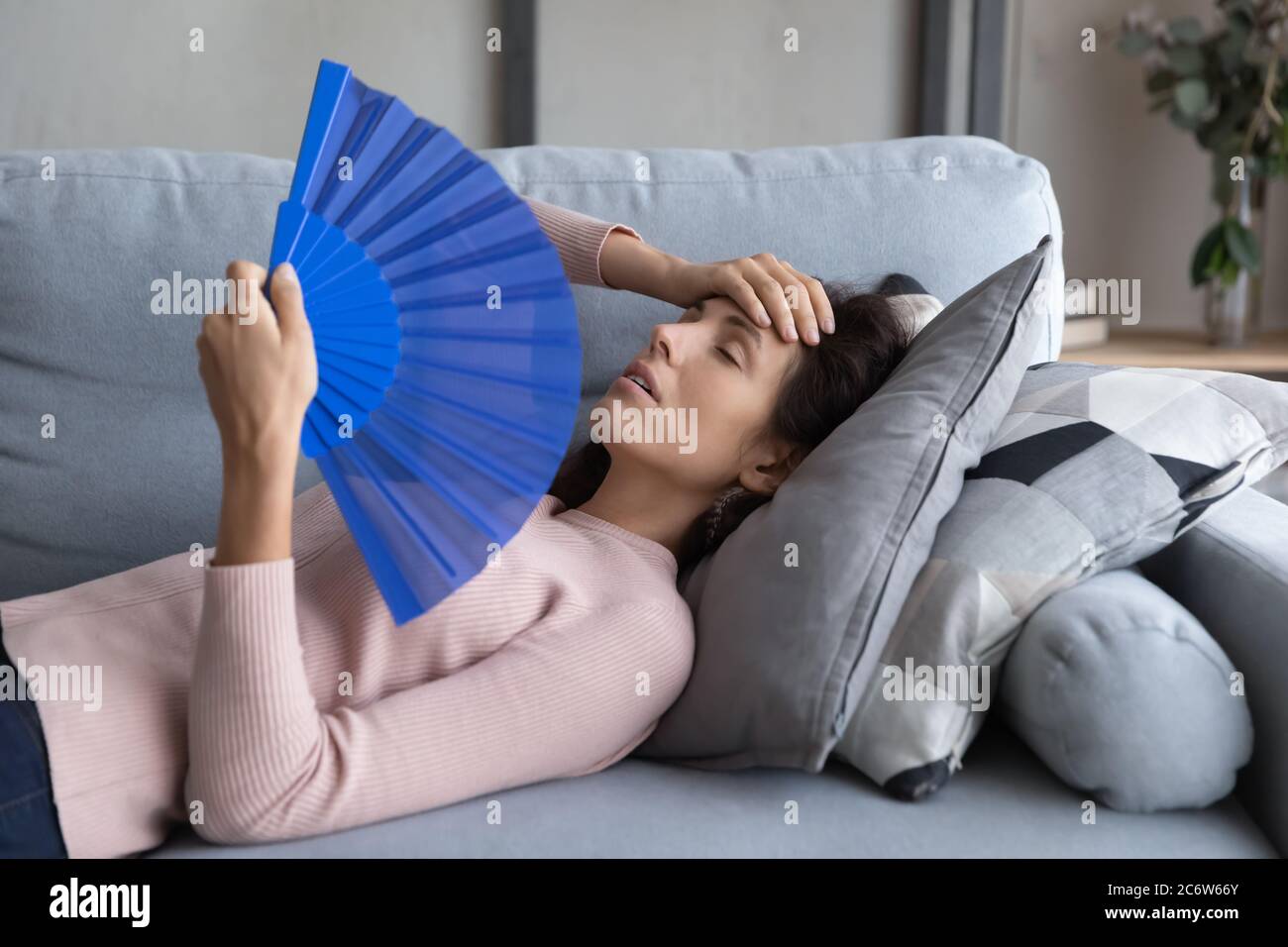 Überhitzte junge Frau entspannen auf Sofa Welle mit Handventilator Stockfoto