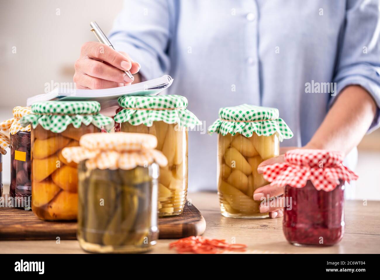 Hausgemachte Obst und eingelegtes Gemüse mit einer Frau, die das Rezept im Hintergrund aufschreibt. Stockfoto