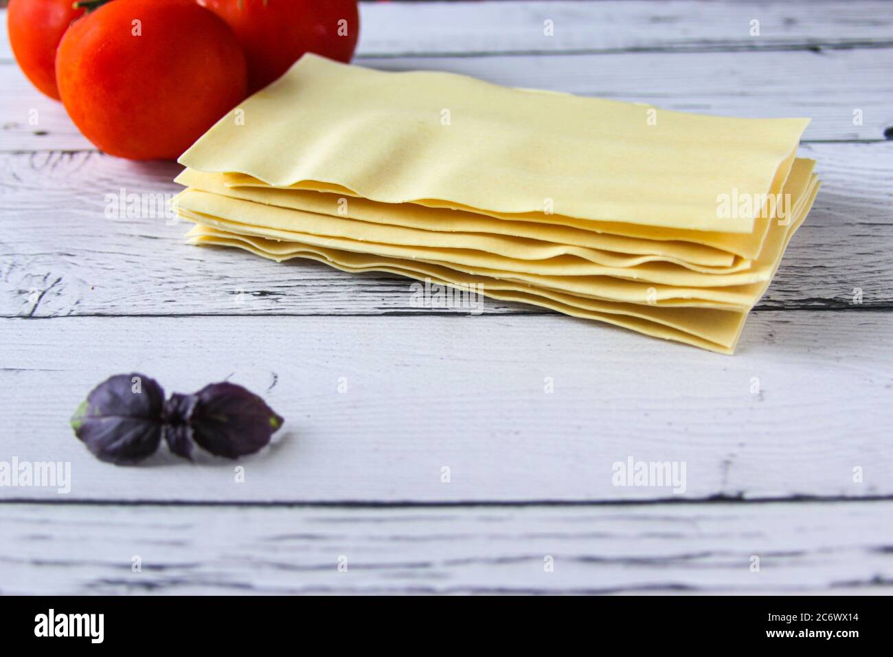 Lasagne Blätter Pasta mit Tomaten und Basilikum Blatt auf einem Holzhintergrund. Zutaten für ein italienisches Rezept. Speicherplatz kopieren. Stockfoto